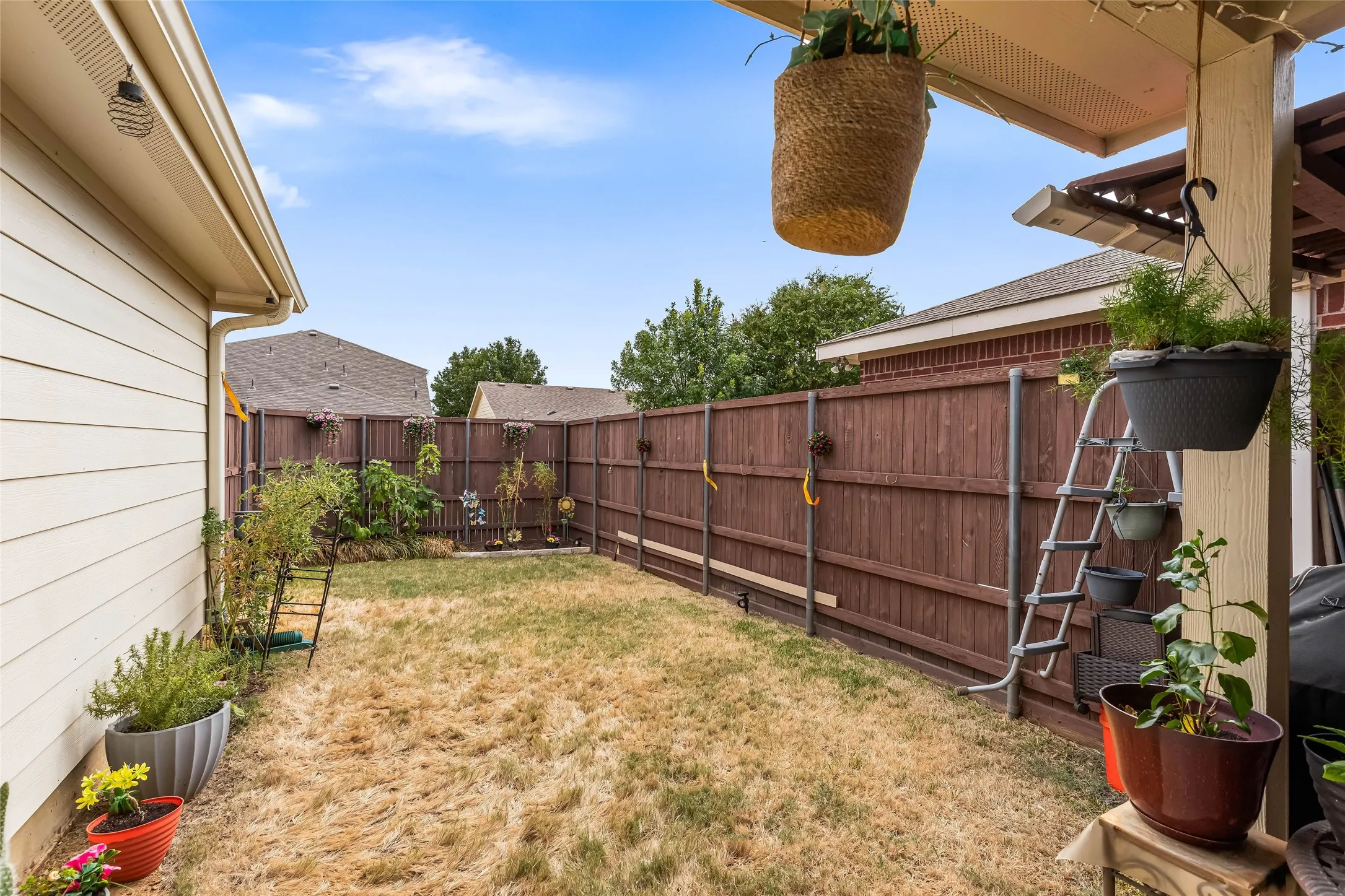 Small enclosed backyard features a privacy fence, a small covered patio area, and an additional covered open area storage area for tools, equipment, etc.