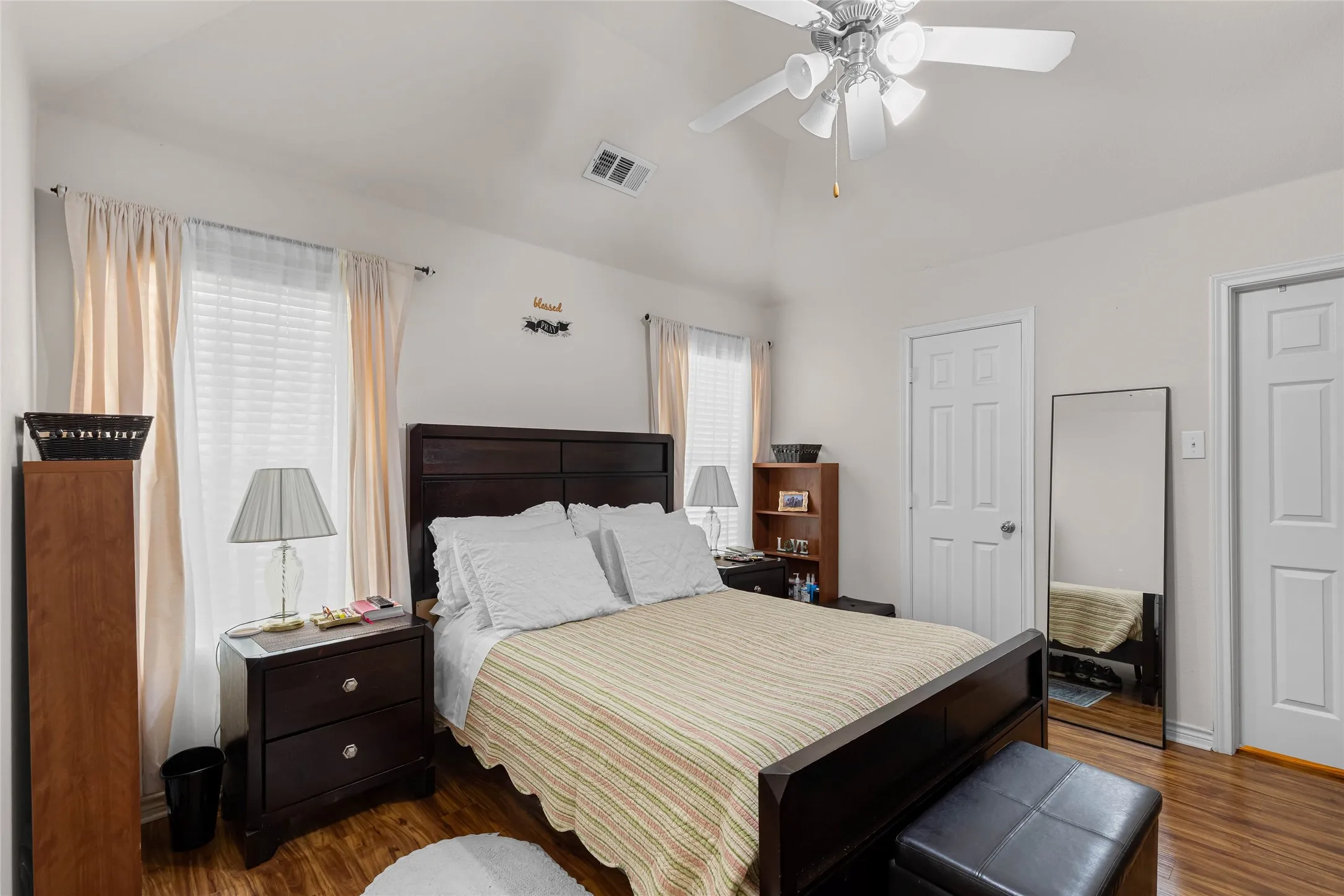 Vaulted ceiling with a ceiling fan, dual windows with blinds, wood-finish flooring, and walk in closet and full bathroom.