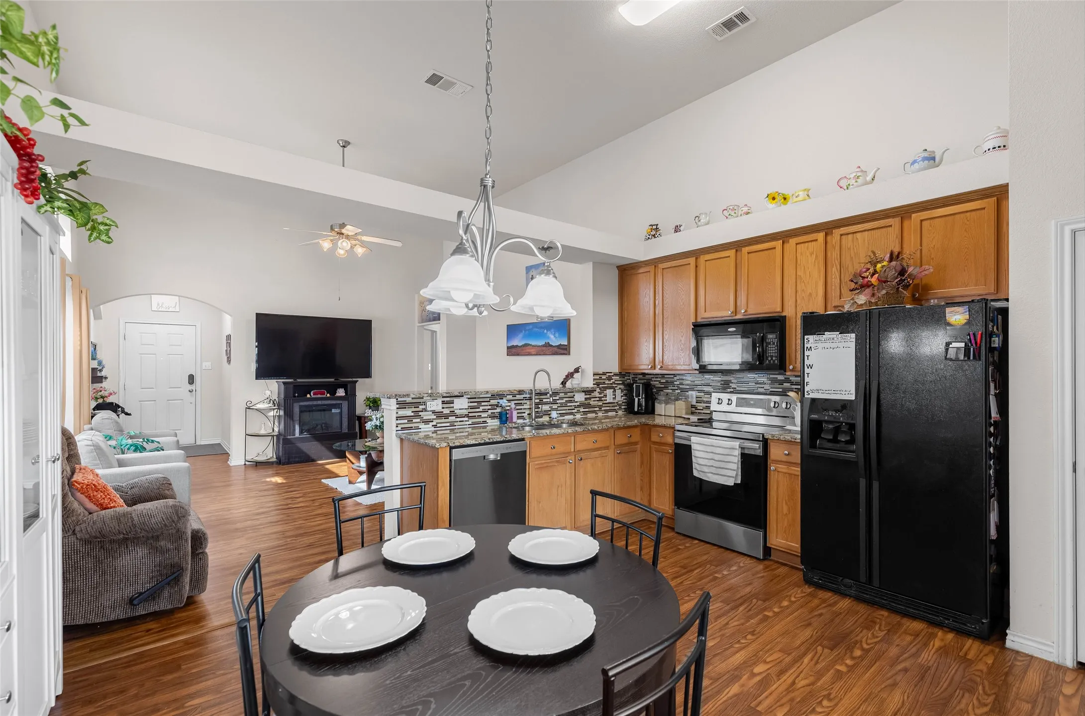 Vaulted ceilings, wood-finish flooring, and a kitchen featuring wood cabinetry, stainless steel appliances, and a mosaic tile backsplash