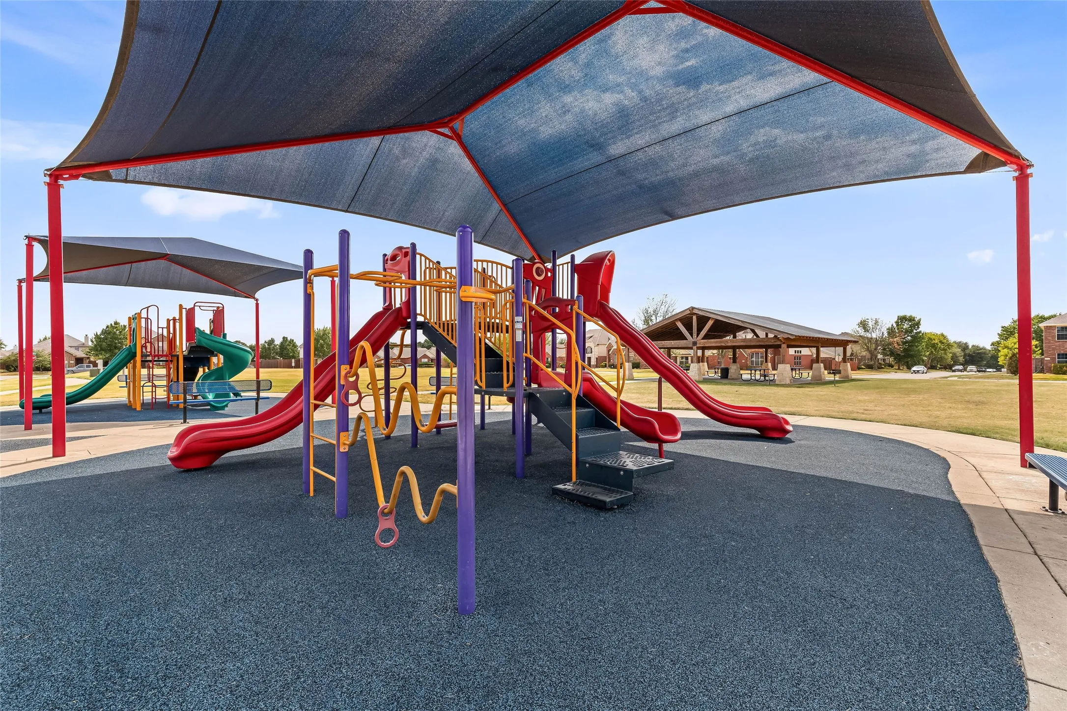 Community playgrounds located just across the street with multiple slides, climbing structures, shade canopy, and soft ground cover.
