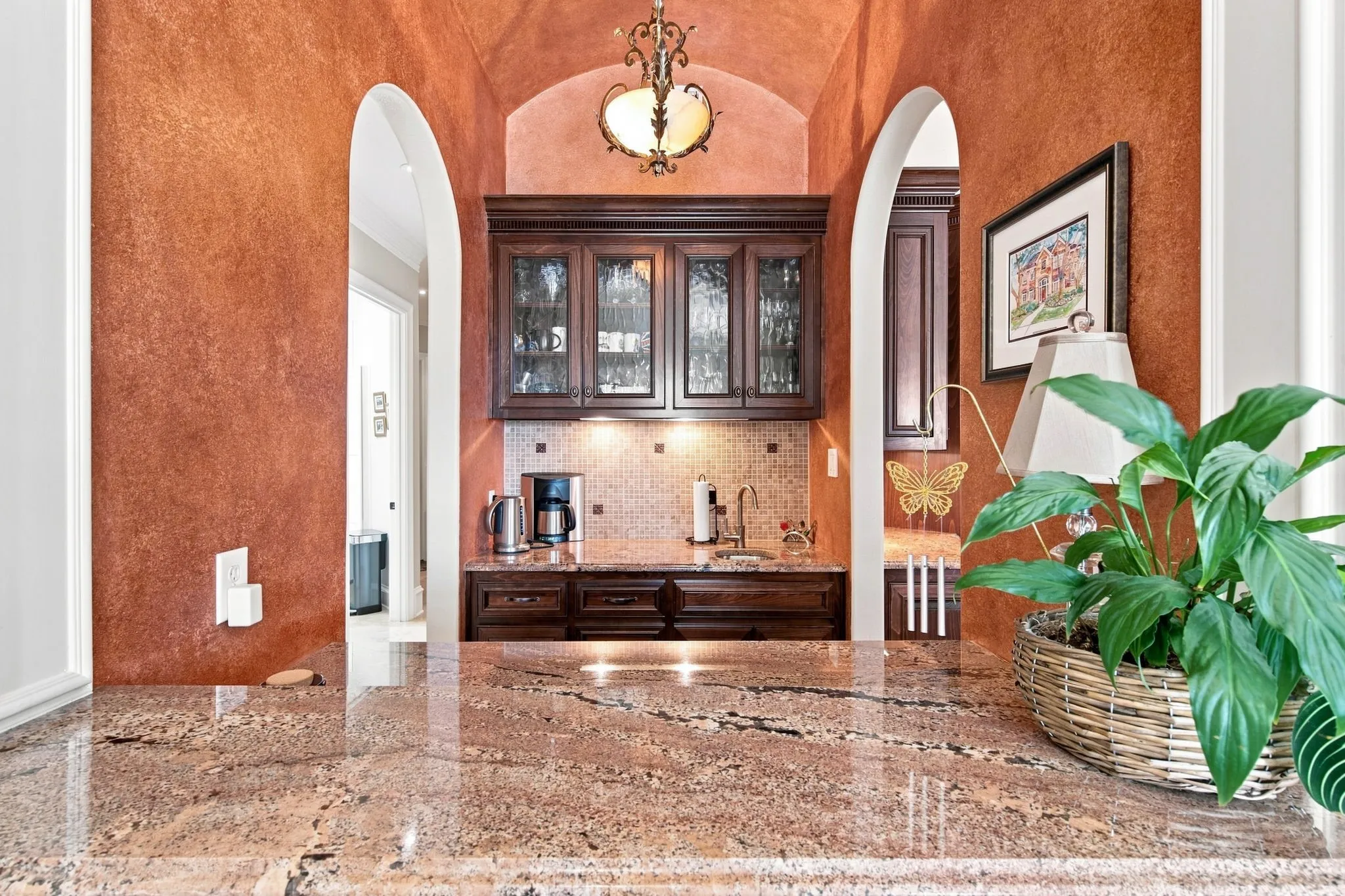 Built-in bar area featuring arched doorways, dark wood cabinetry with glass fronts, a tile backsplash, and polished stone countertops