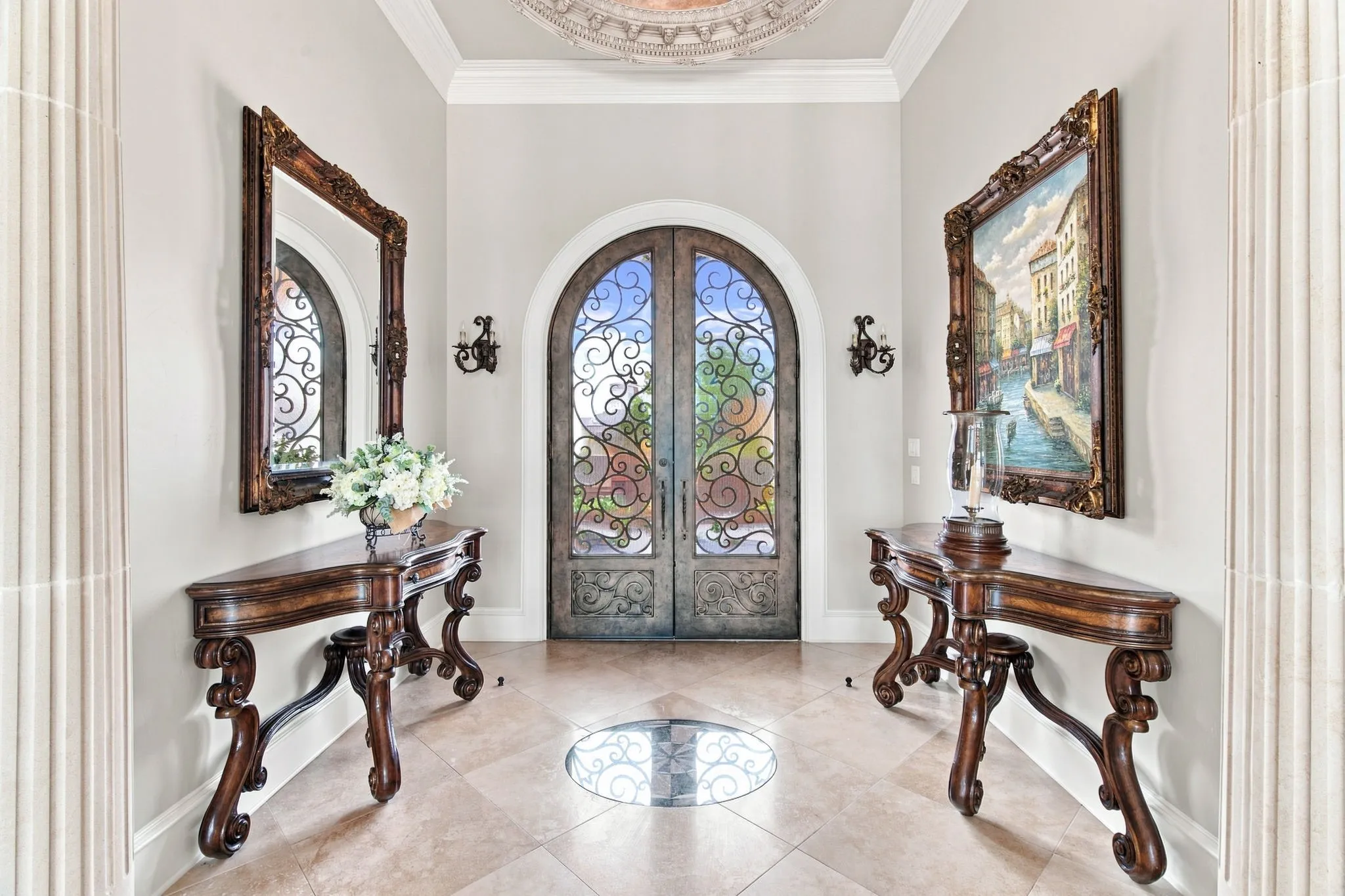 Arched entryway with ornate ironwork double doors, tile flooring with a decorative inlay, crown molding, and fluted architectural columns