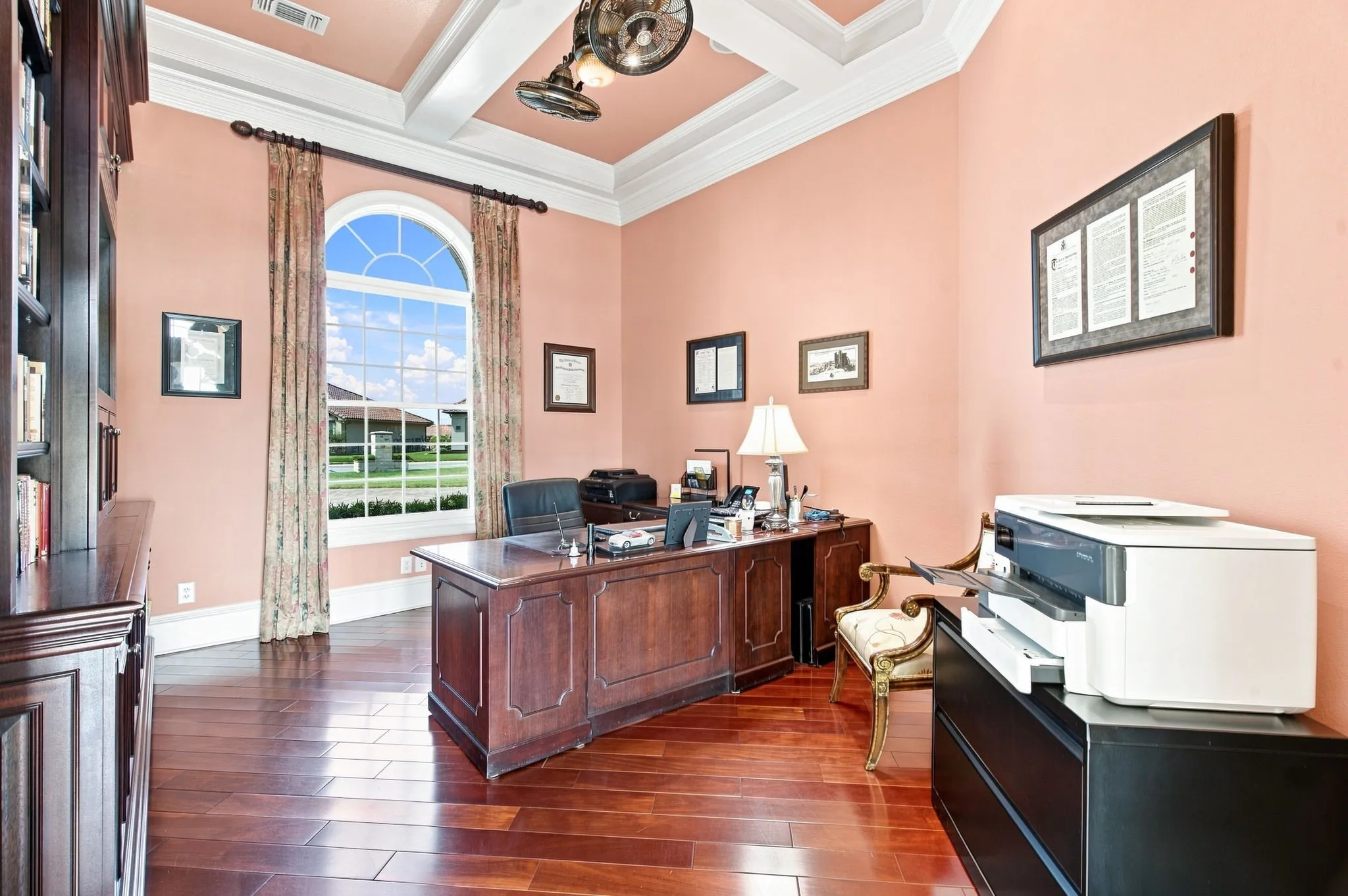 Arched window, wood-finish flooring, built-in shelving, coffered ceiling, and crown molding