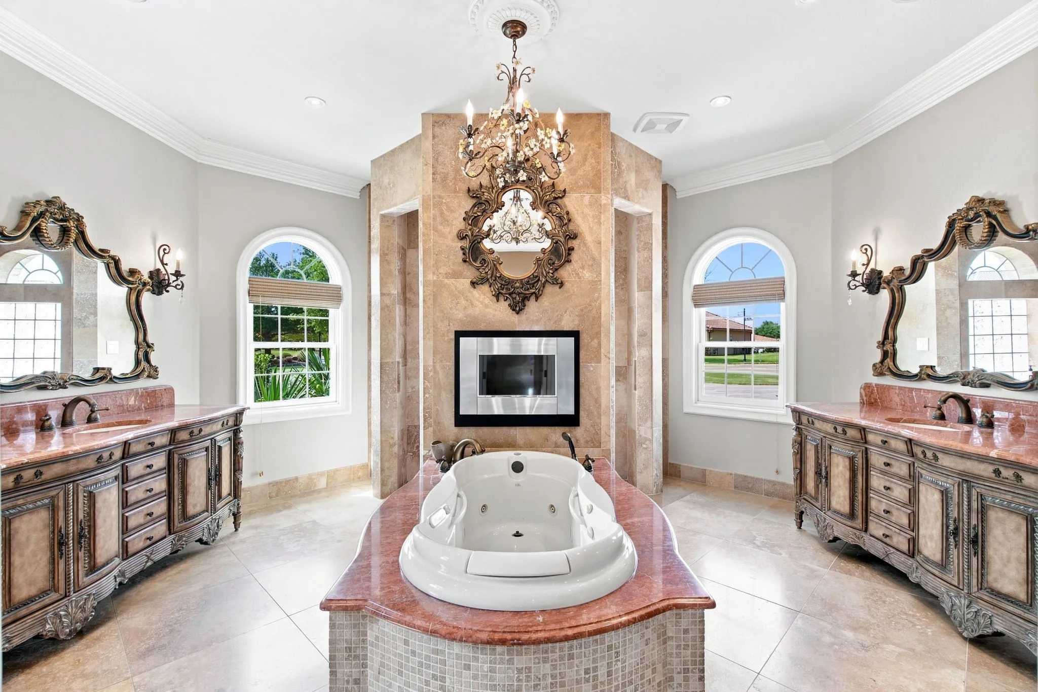 Freestanding soaking tub with a tiled surround, dual vanity stations with ornate mirrors, and arched windows