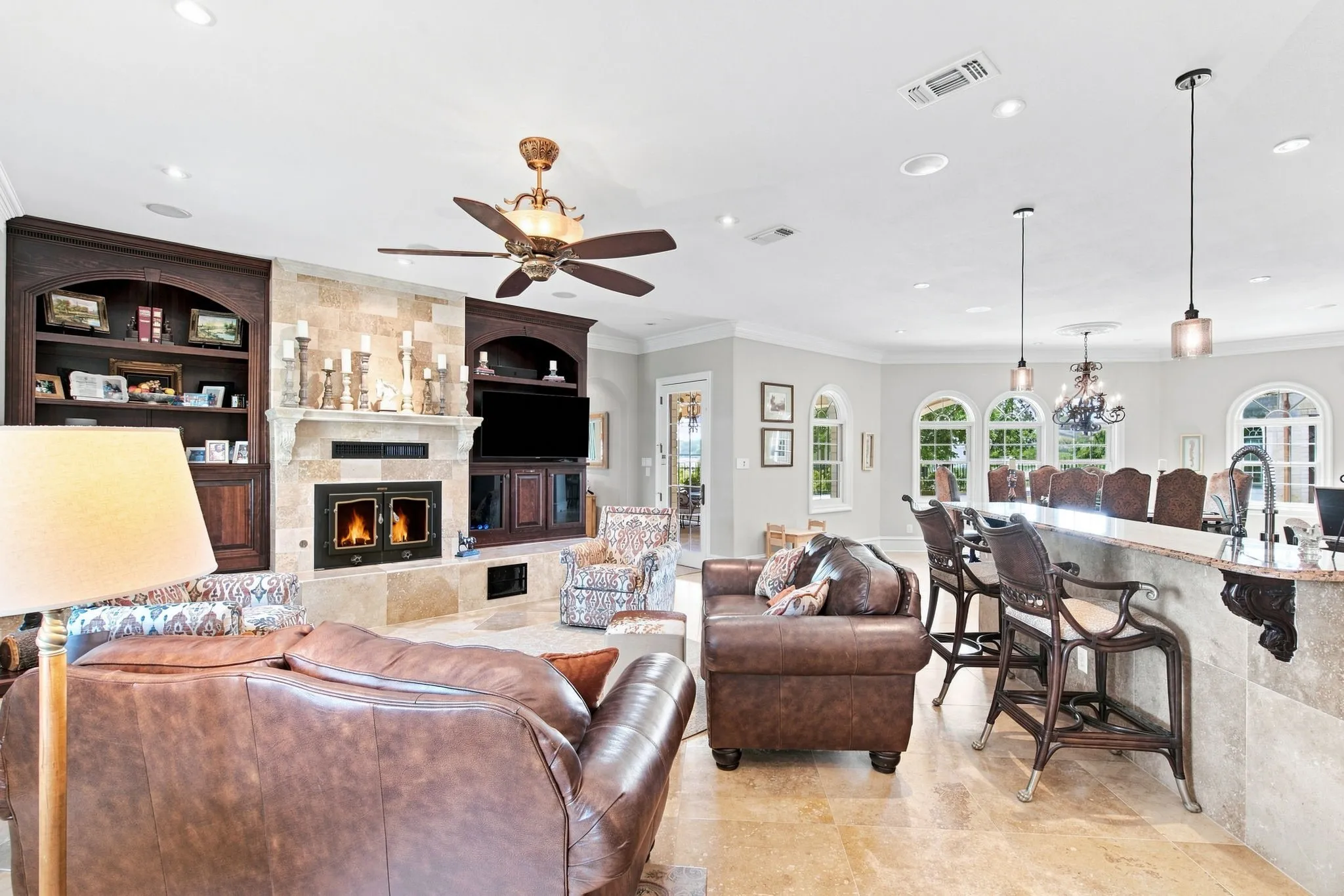 Stone-clad fireplace with built-in dark wood cabinetry, ceiling fan, recessed lighting, and stone-finish flooring