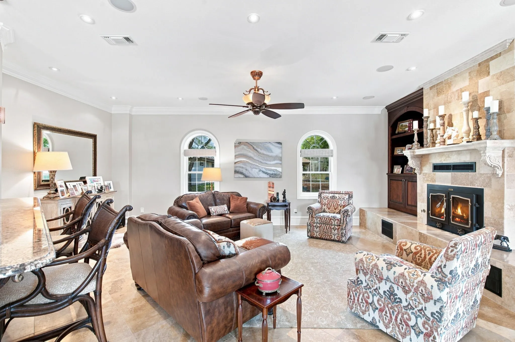 Recessed lighting, crown molding, arched windows, built-in cabinetry, and a stone fireplace with hearth