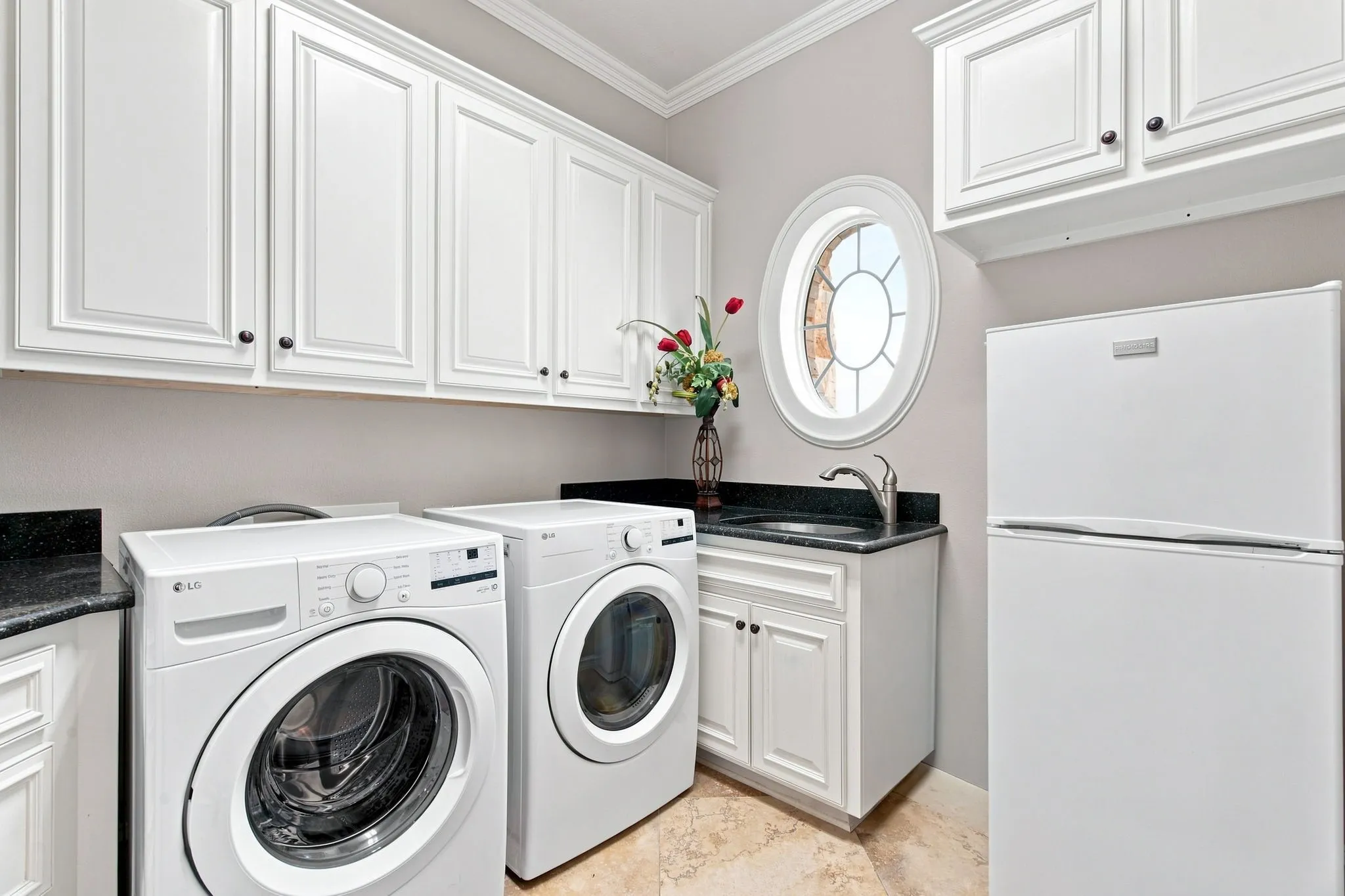White cabinetry with dark hardware, granite countertops, oval window with decorative muntins, and tiled flooring