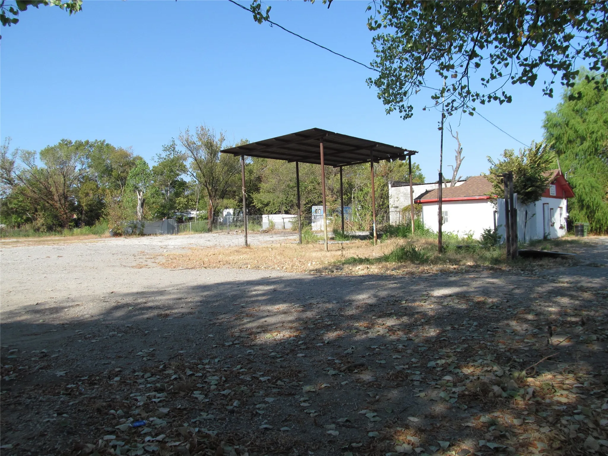 Detached structure with white siding and red trim, concrete foundation, and a metal carport structure