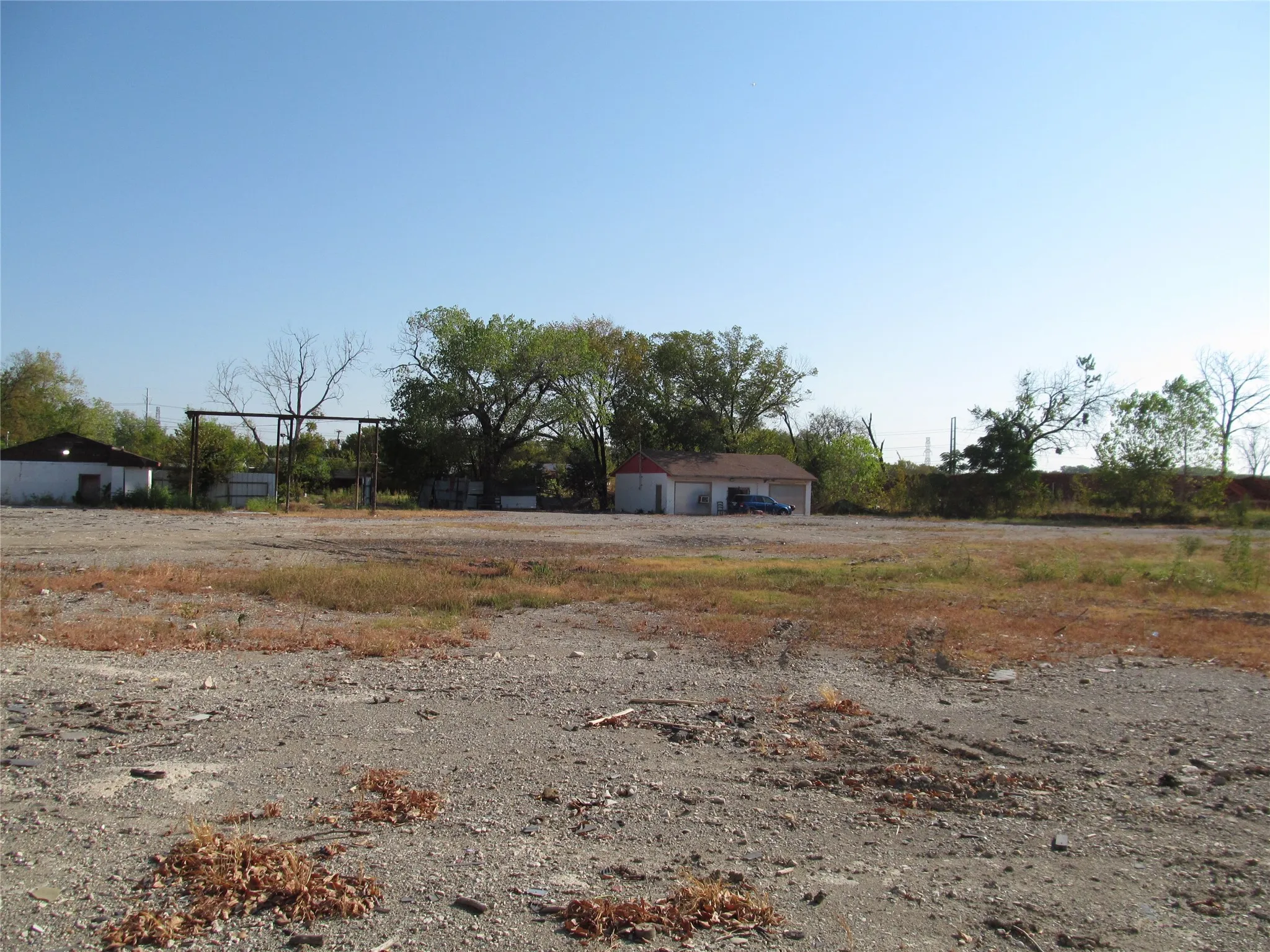 Expansive gravel lot with a detached white building featuring a red roof and a second white structure with a dark roof