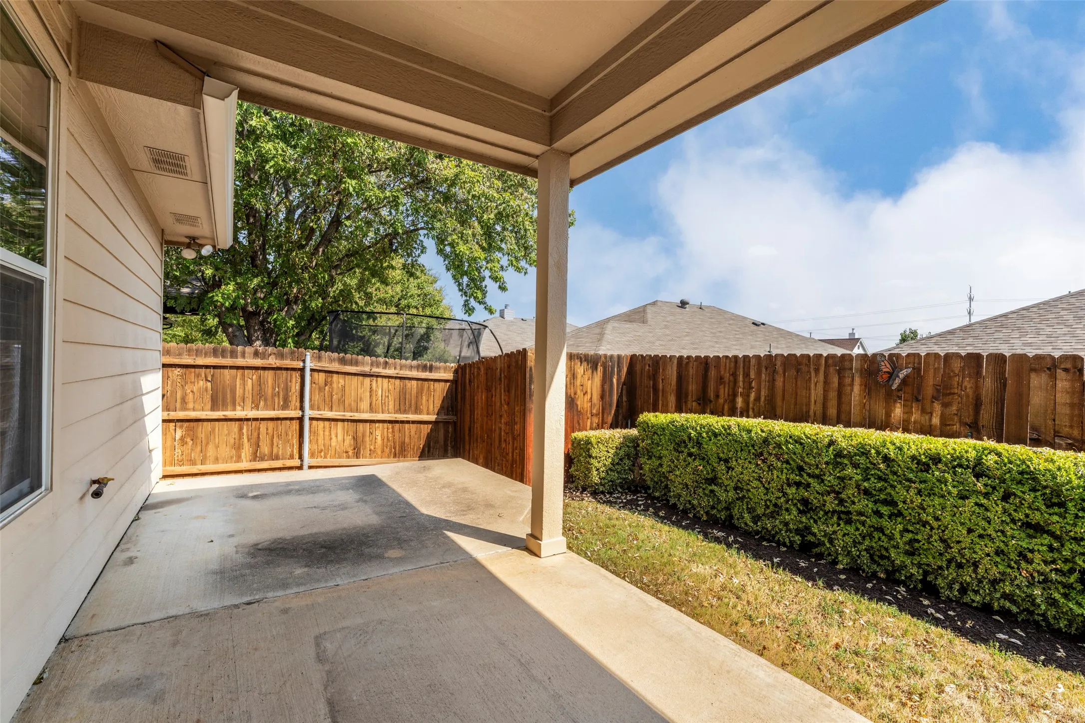 Covered patio with concrete flooring, wood privacy fencing, and manicured shrubbery