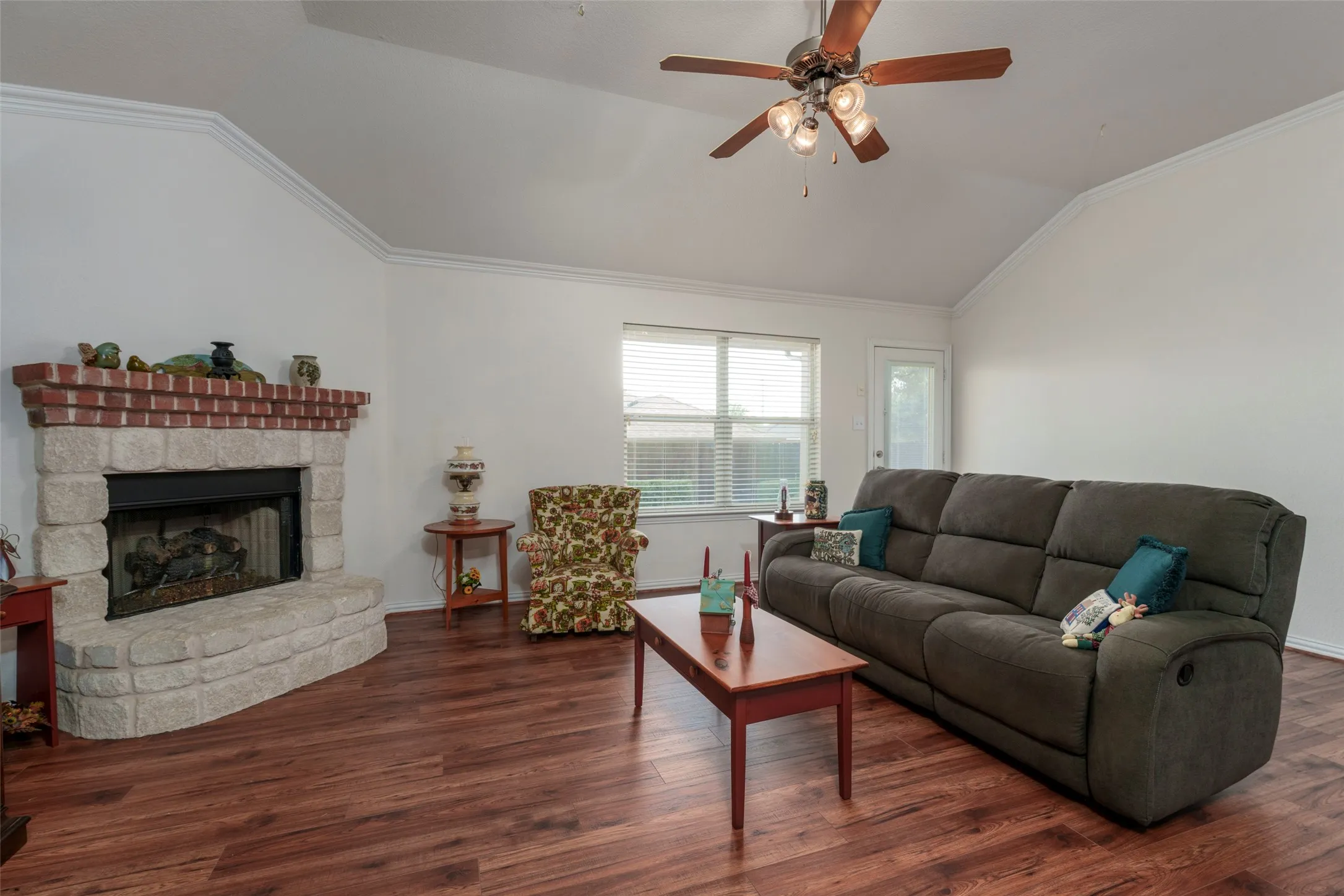 Vaulted ceiling featuring a ceiling fan, crown molding, brick and stone fireplace, and wood-finish flooring