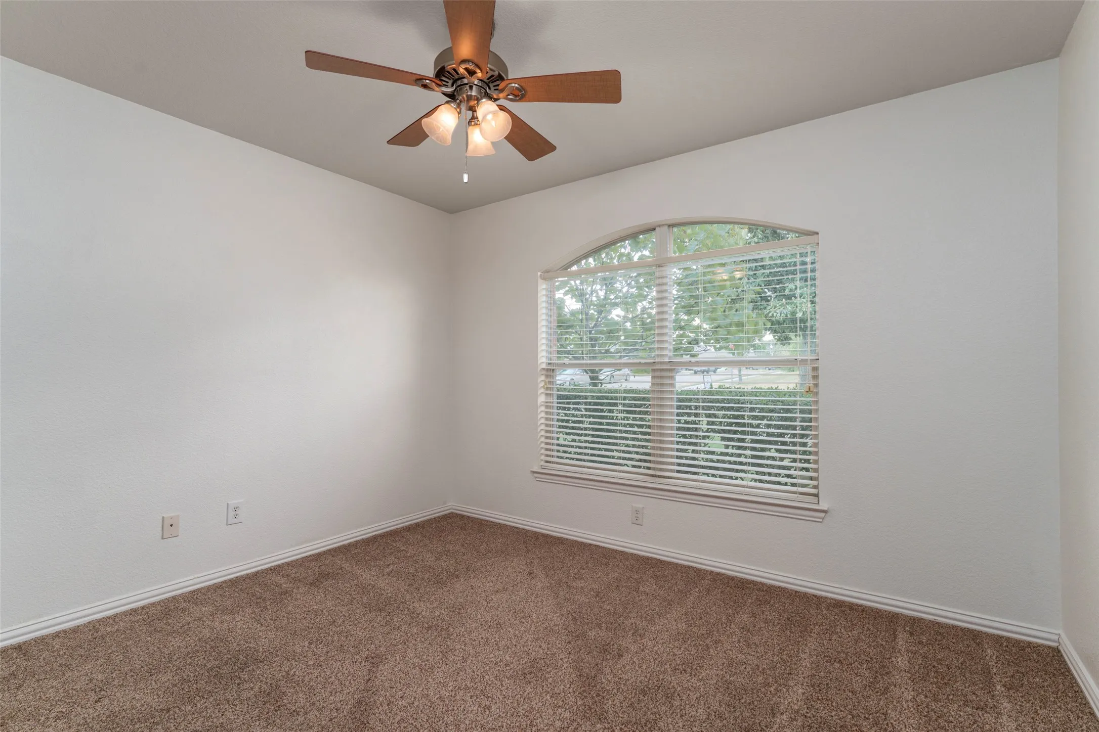 Arched window with blinds, ceiling fan with integrated lighting, and neutral carpet flooring