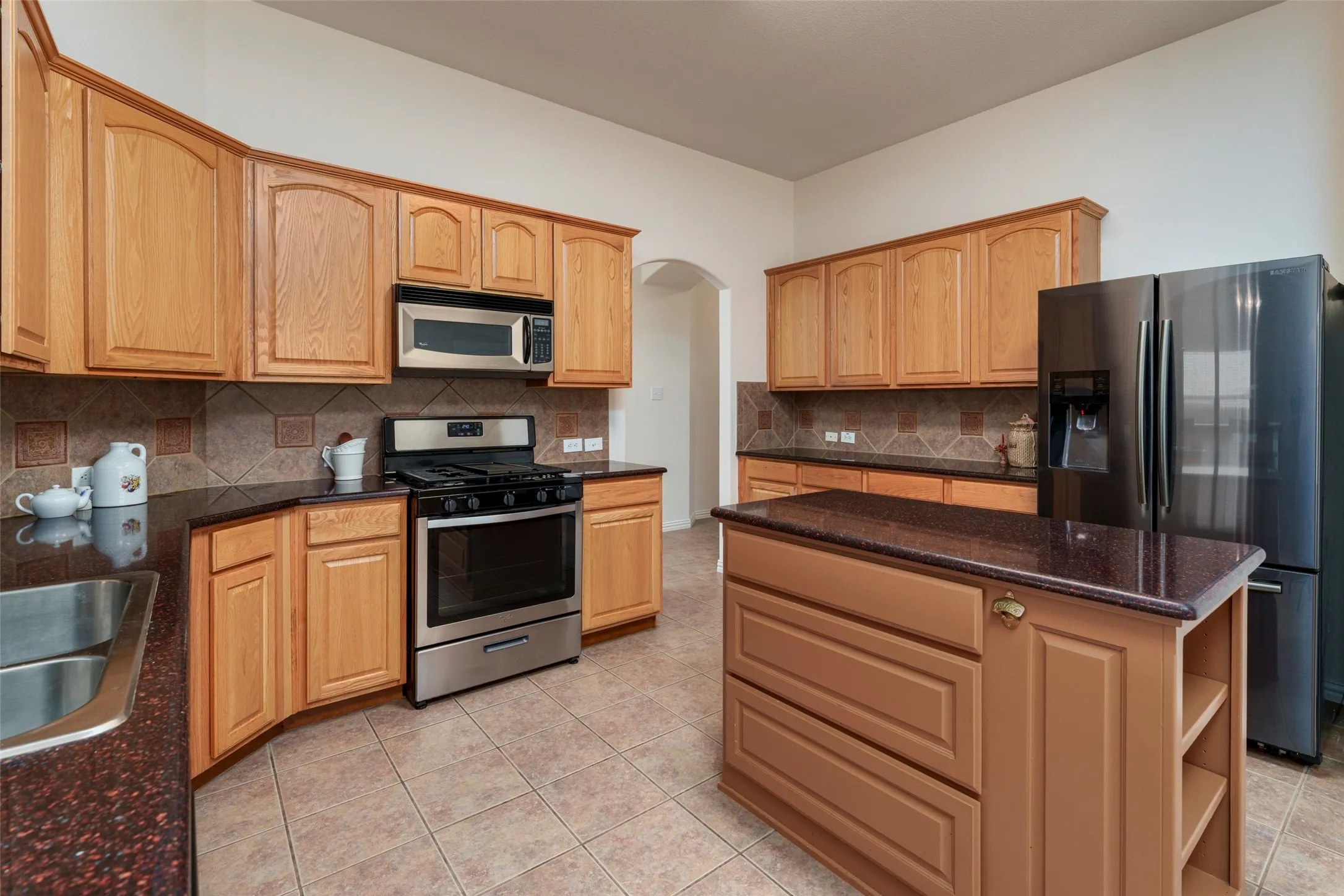 Kitchen featuring wood cabinetry, stainless steel appliances, a center island with countertop, tiled flooring, and a tiled backsplash