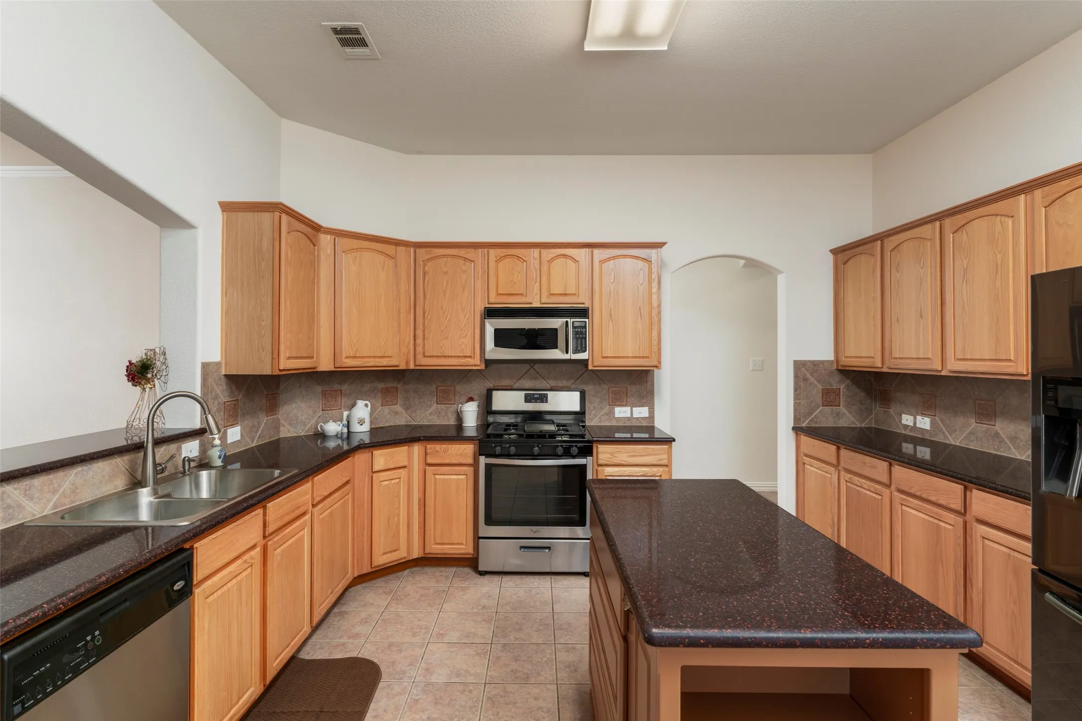 Kitchen featuring stainless steel appliances, wood cabinetry, dark countertops, a tile backsplash, and a central island