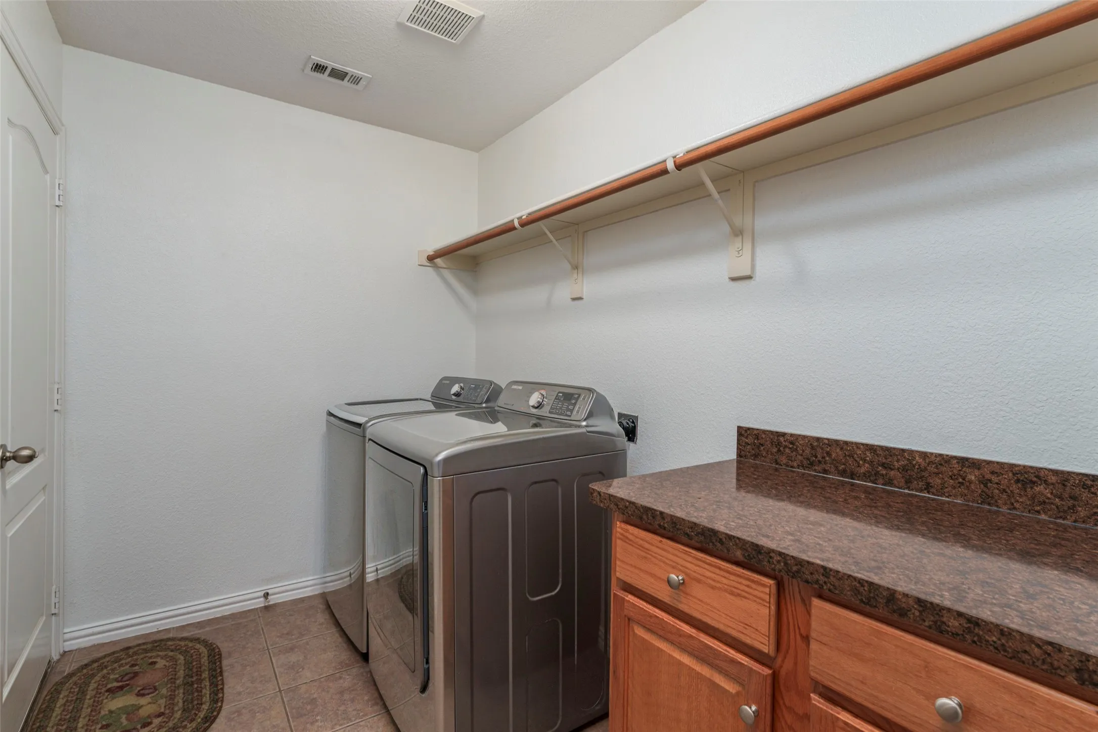 Laundry area featuring built-in cabinetry, durable countertop, and a clothes hanging rod with shelving