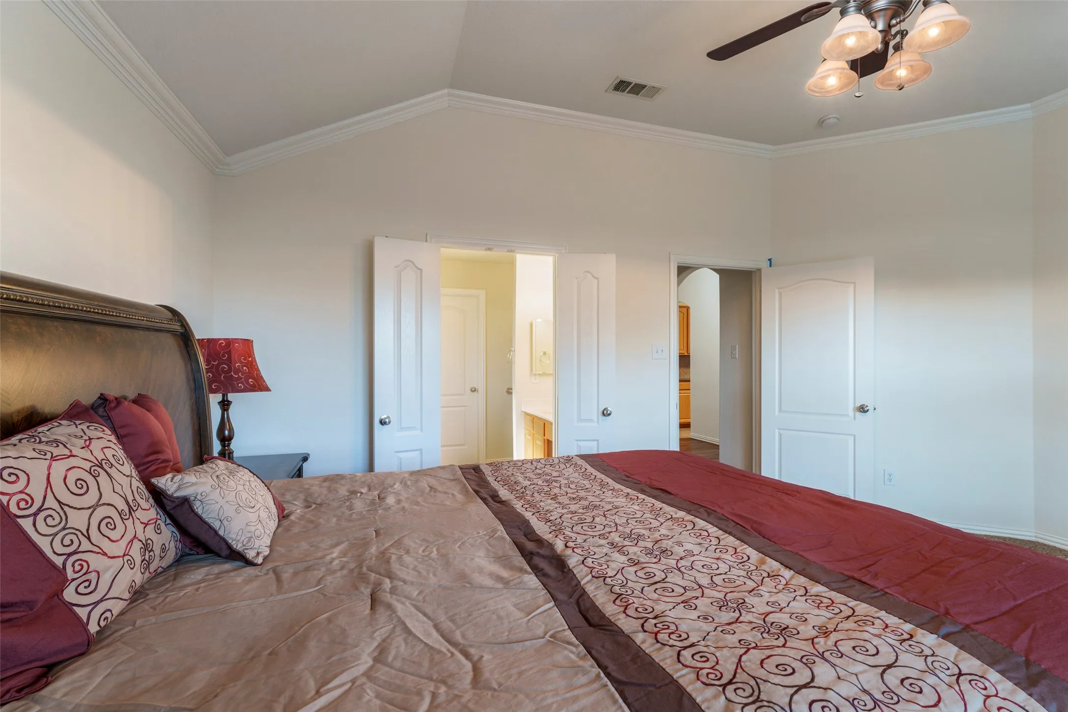 Vaulted ceiling with crown molding, ceiling fan with integrated lighting, wood-finish flooring, white panel doors