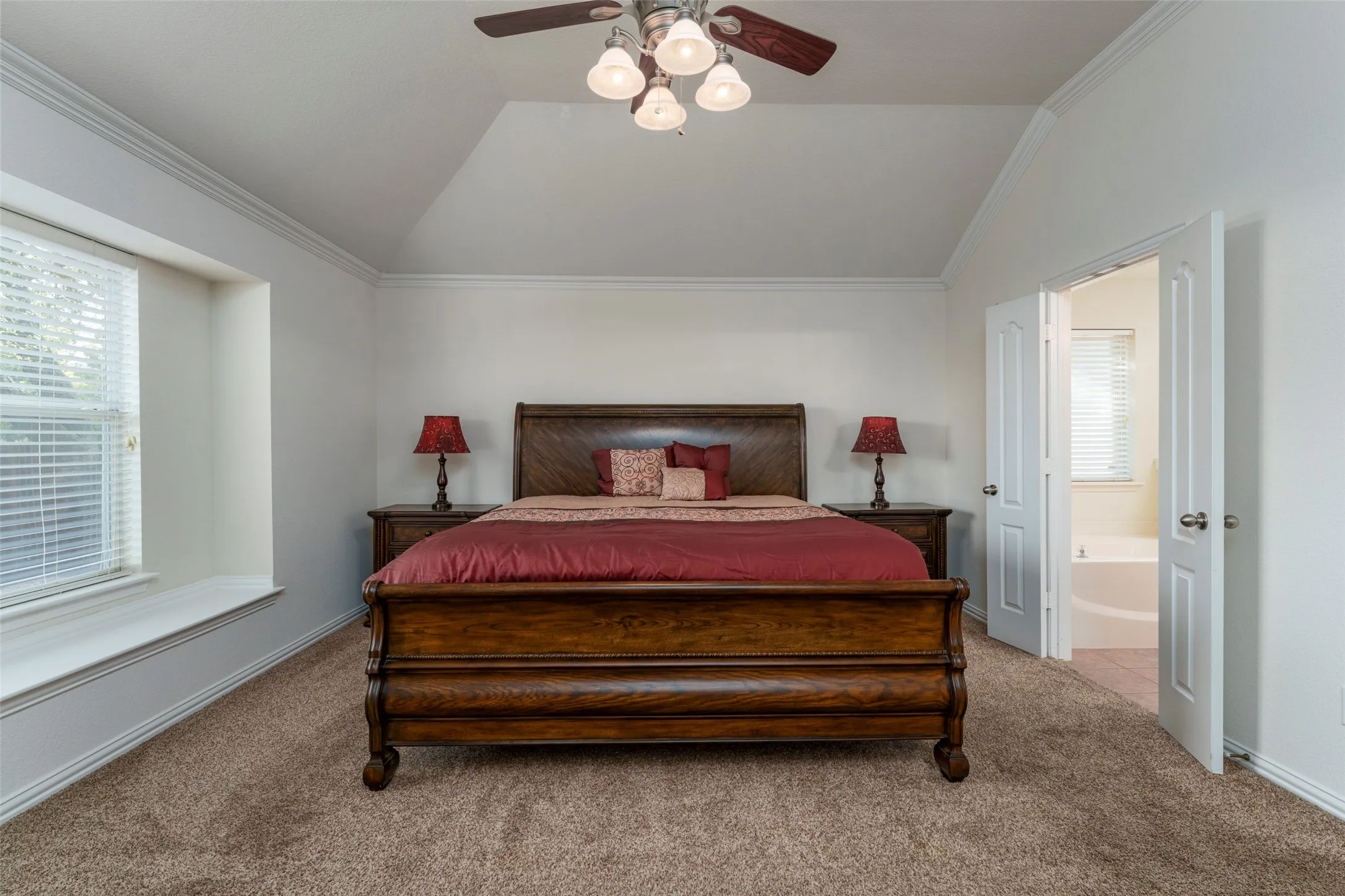 Vaulted ceiling with crown molding, window with deep sill, double doors, and ceiling fan with lighting