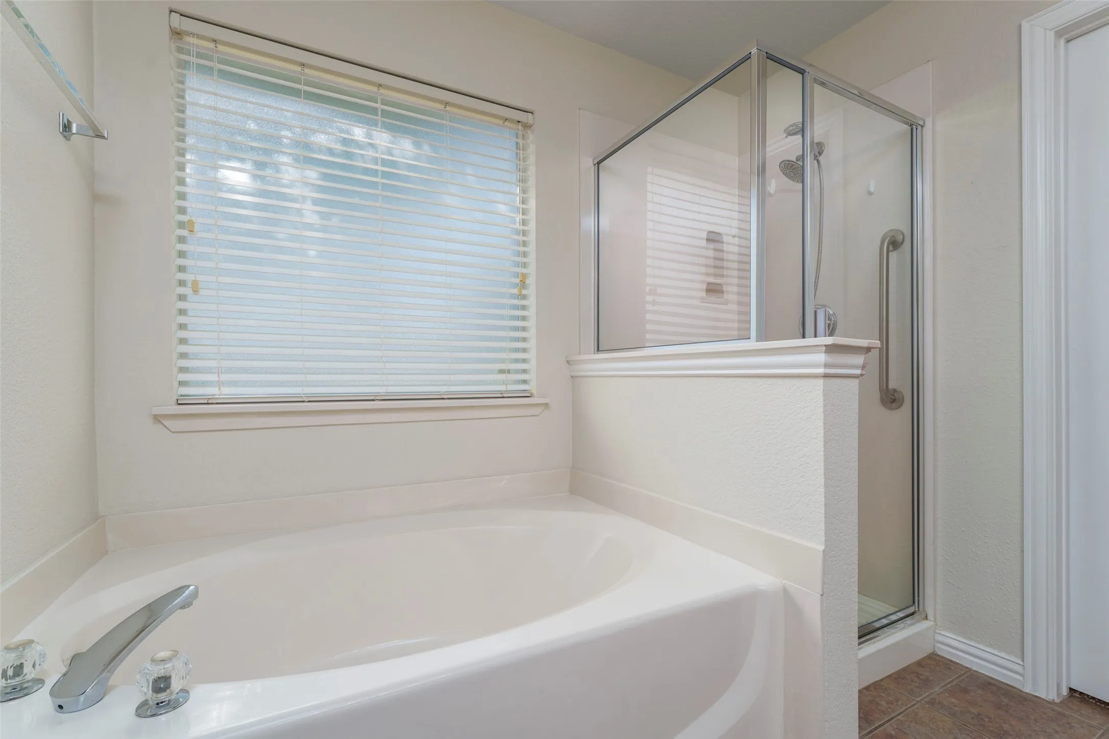 Soaking tub with chrome fixtures, an adjacent glass-enclosed shower, and a window with horizontal blinds