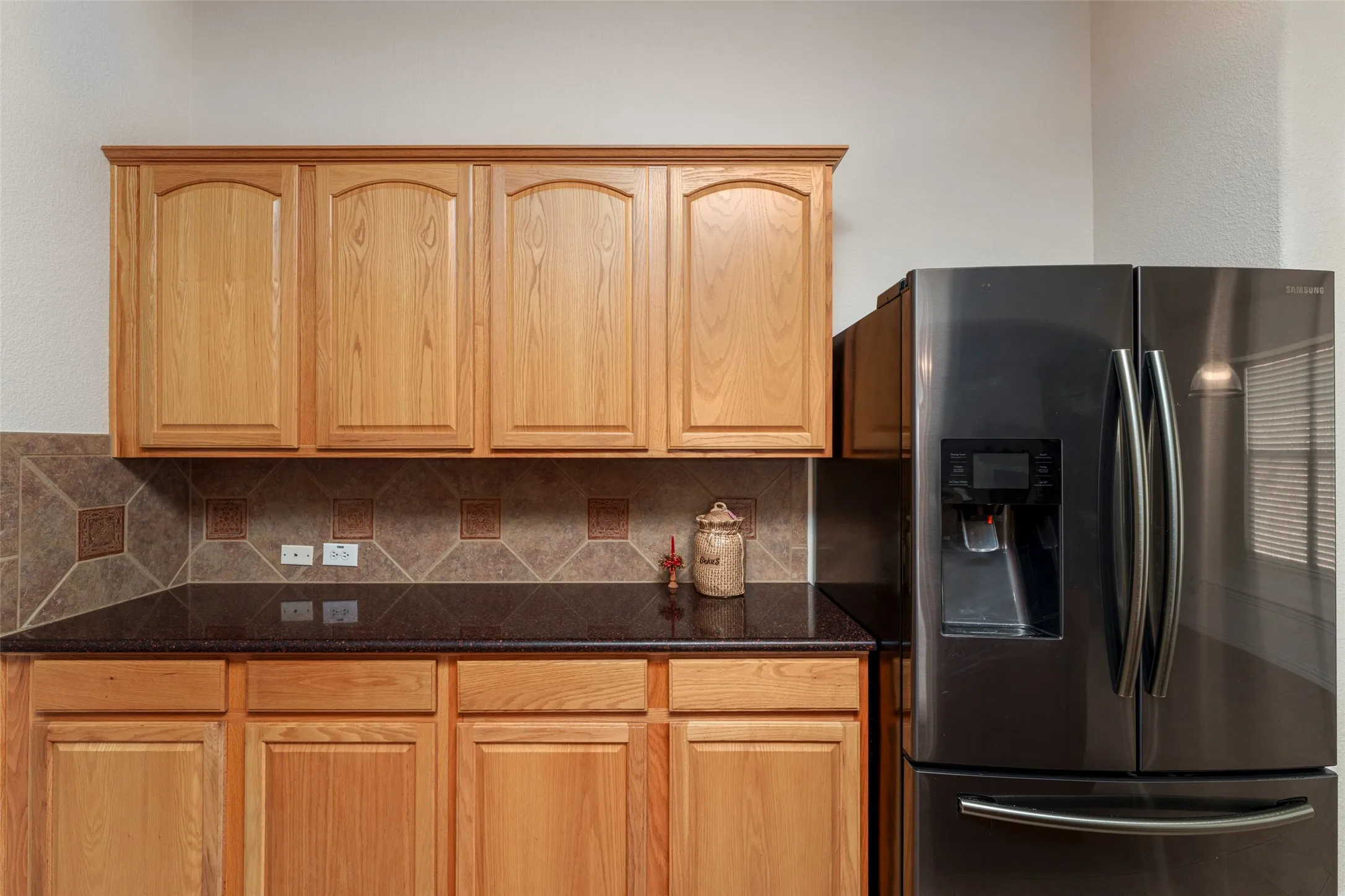 Wood-finish cabinetry, dark countertop, and tiled backsplash