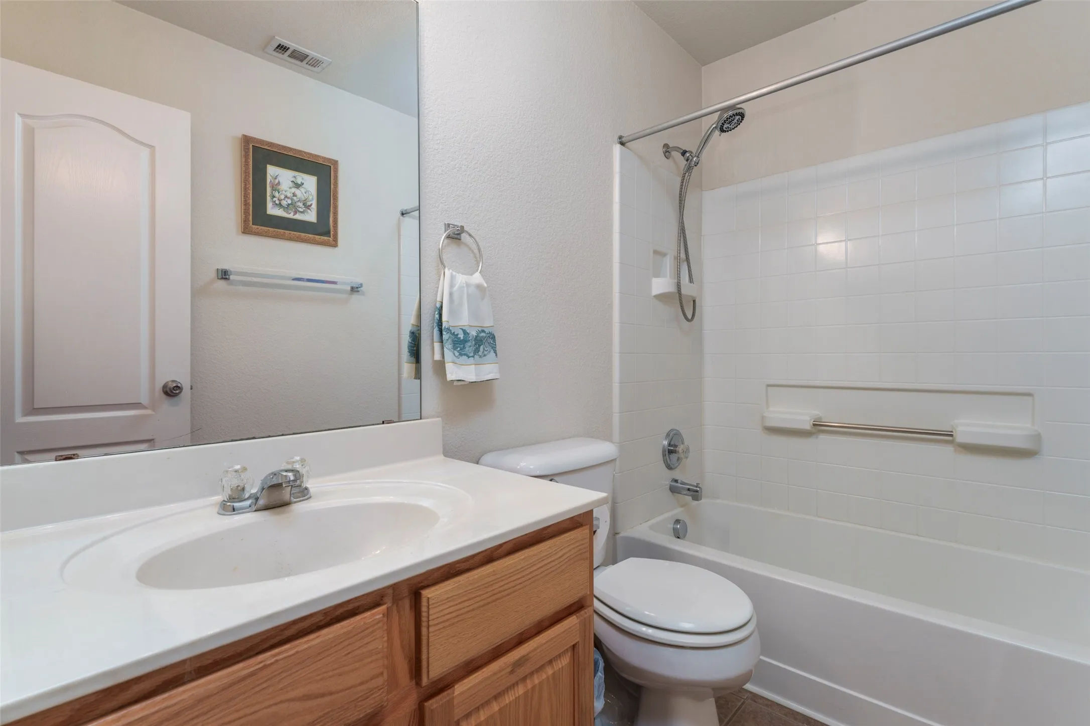 Vanity with integrated sink, wood-finish cabinetry, full-width mirror, and a combination tub/shower with tiled surround