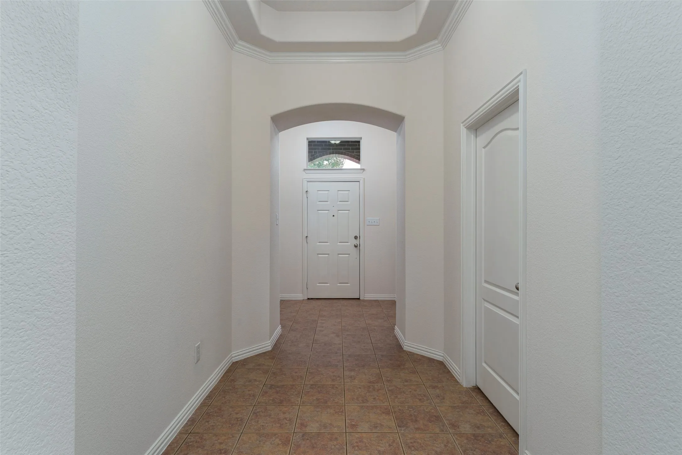 Entryway featuring tile flooring, an arched doorway, and a tray ceiling