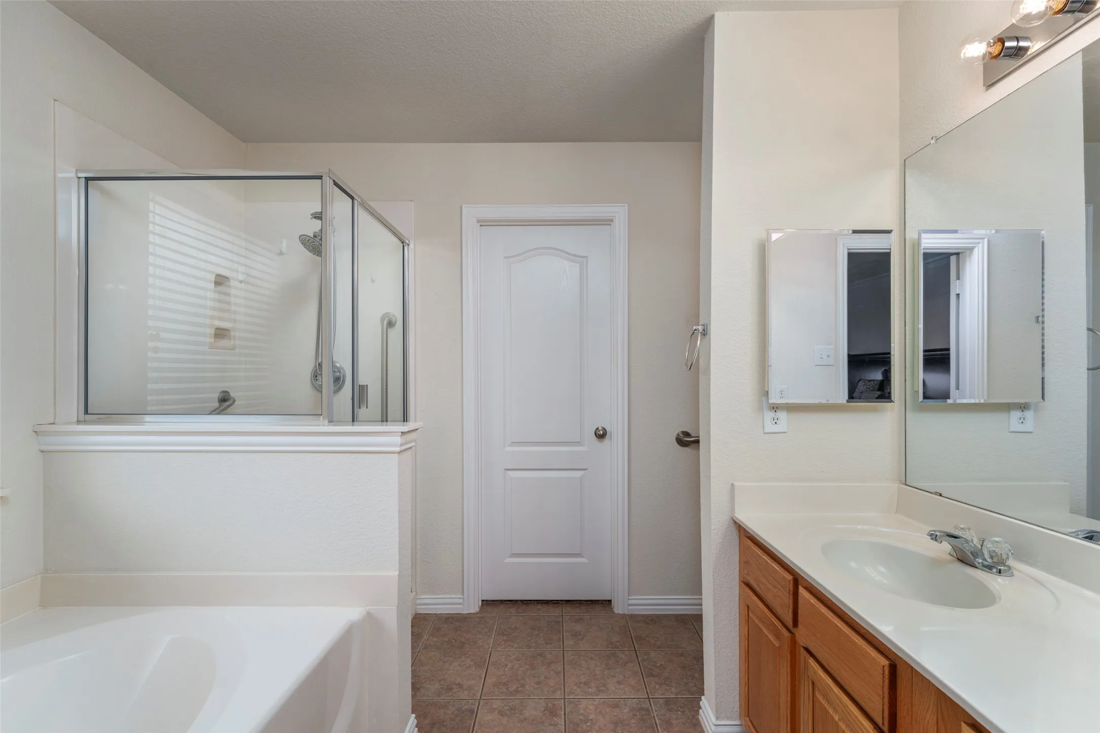 Built-in bathtub, glass-enclosed shower, single vanity with wood cabinetry, large vanity mirror, and neutral tile flooring