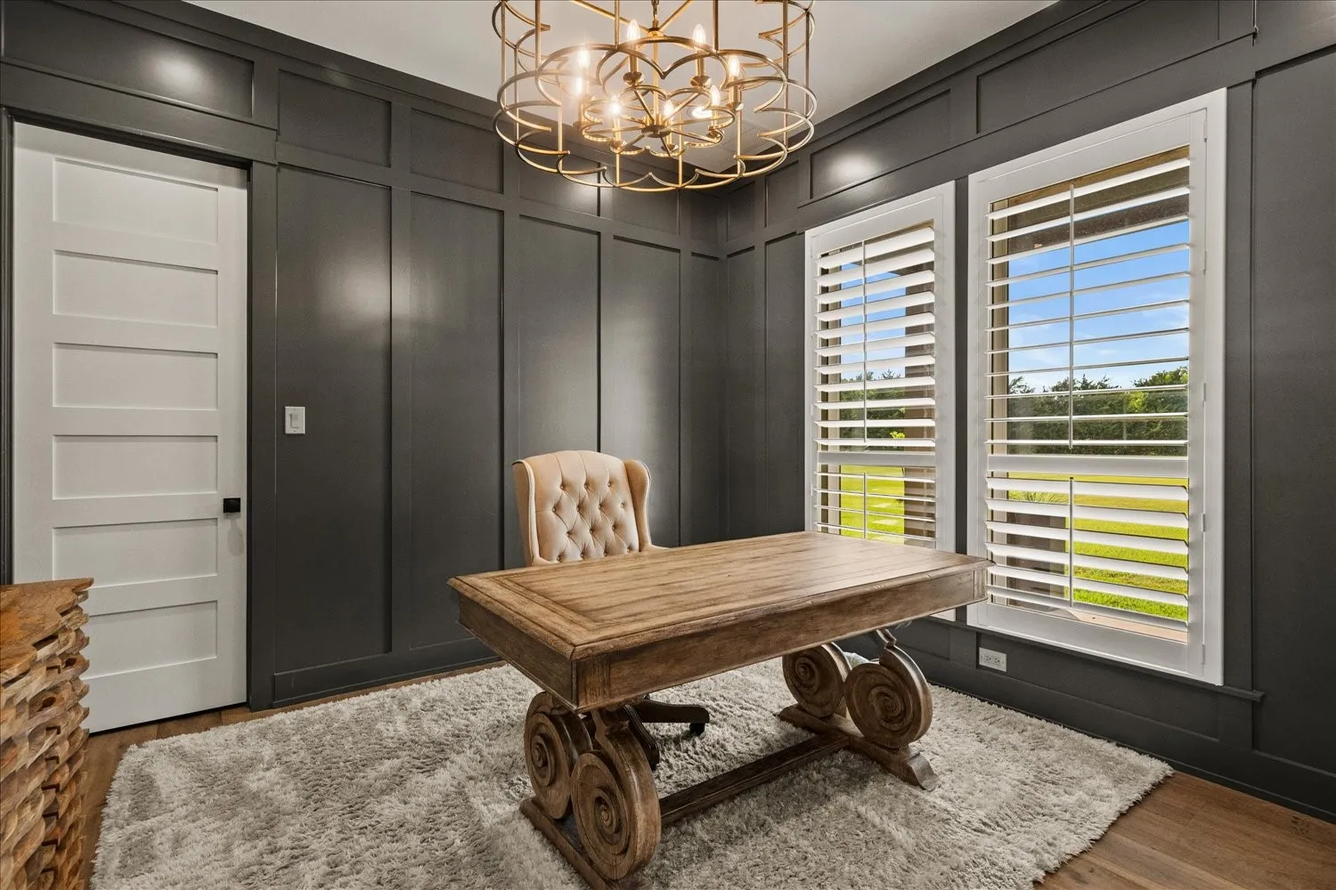 Dark paneled accent walls, two windows with white plantation shutters, wood-finish flooring, and an ornate ceiling light fixture