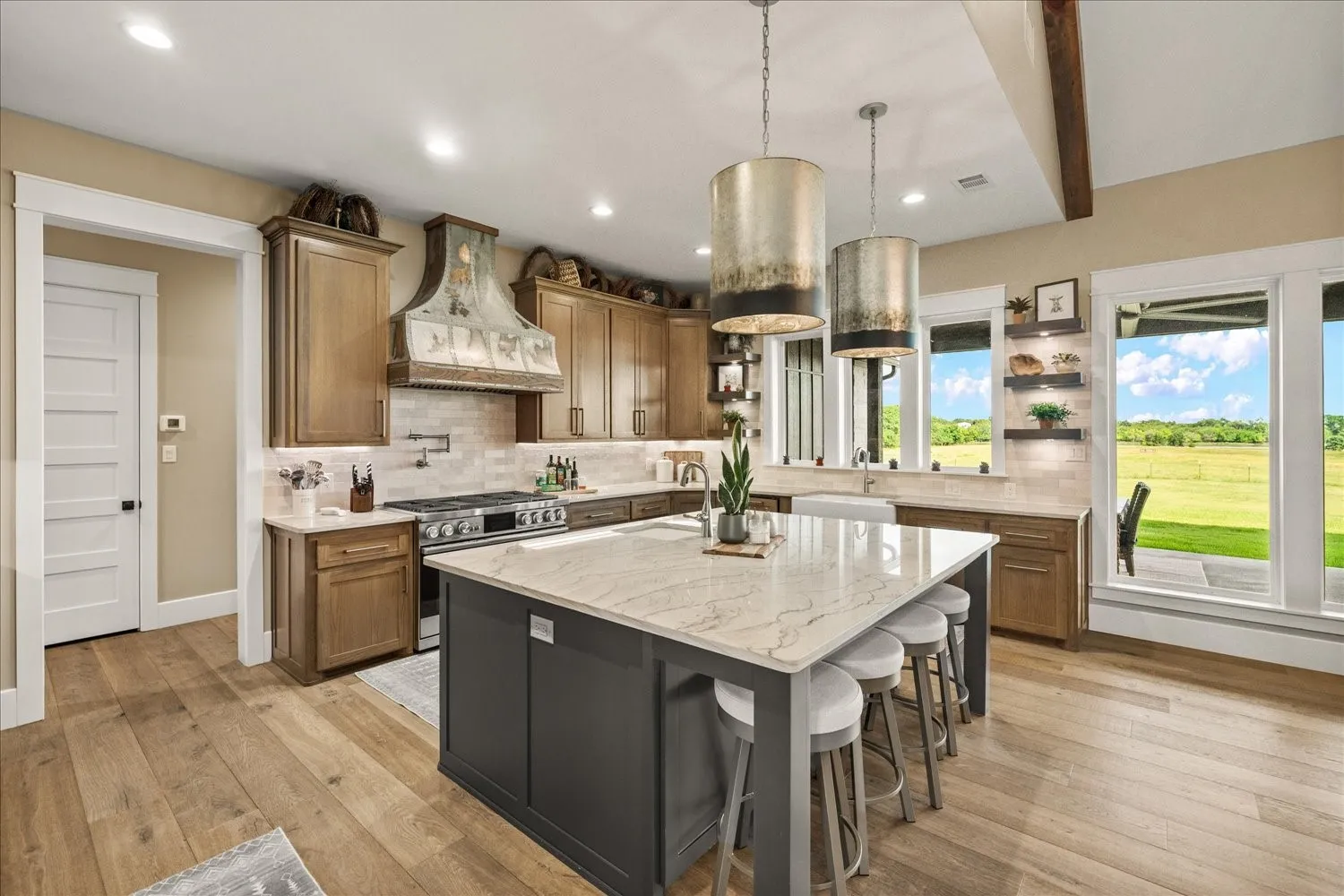 Expansive kitchen featuring a large central island with seating, a professional-grade range with a decorative hood, wood-finish flooring, and a farmhouse sink