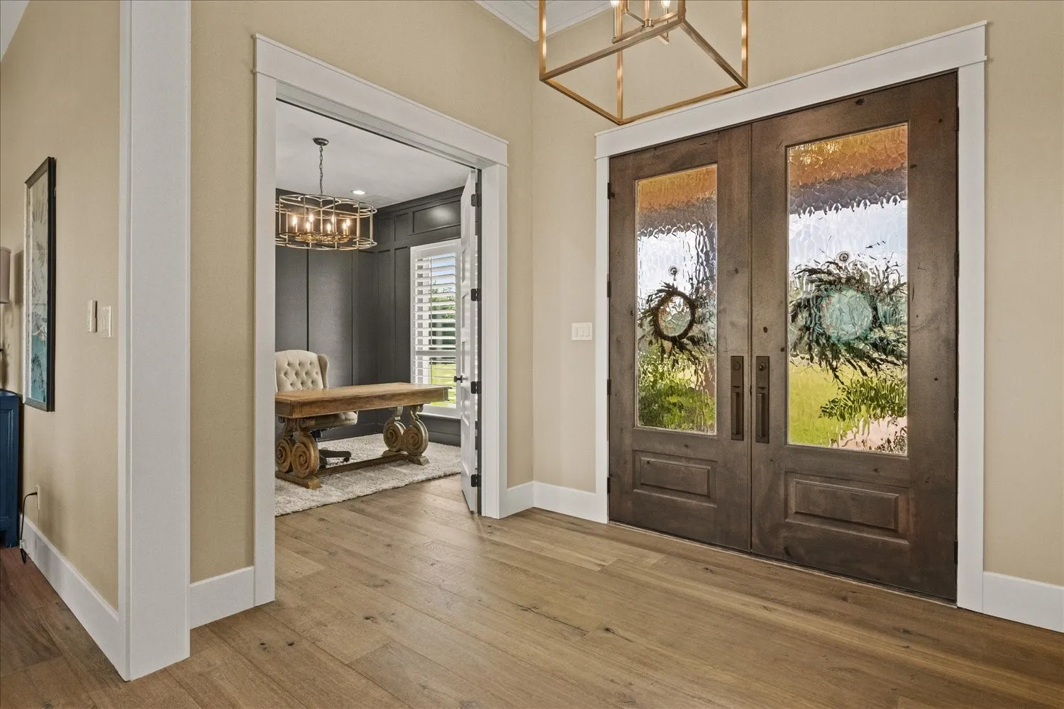 Double entry doors with textured glass panels, light wood-finish flooring, and a decorative overhead light fixture