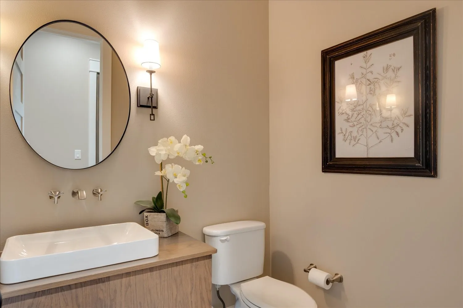 Rectangular vessel sink with wall-mounted faucets, wood-finish vanity, and a circular mirror