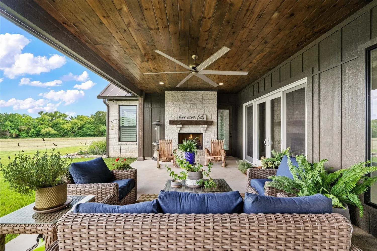 Covered patio with a wood-plank ceiling, ceiling fan, and stone-clad outdoor fireplace