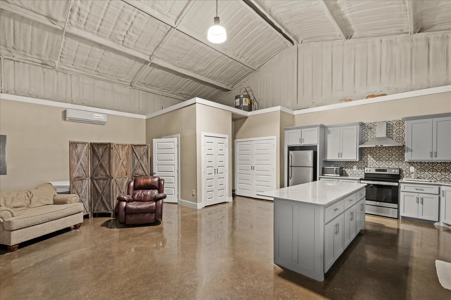 Polished concrete flooring, vaulted ceiling, light gray cabinetry, stainless steel appliances, and a patterned tile backsplash