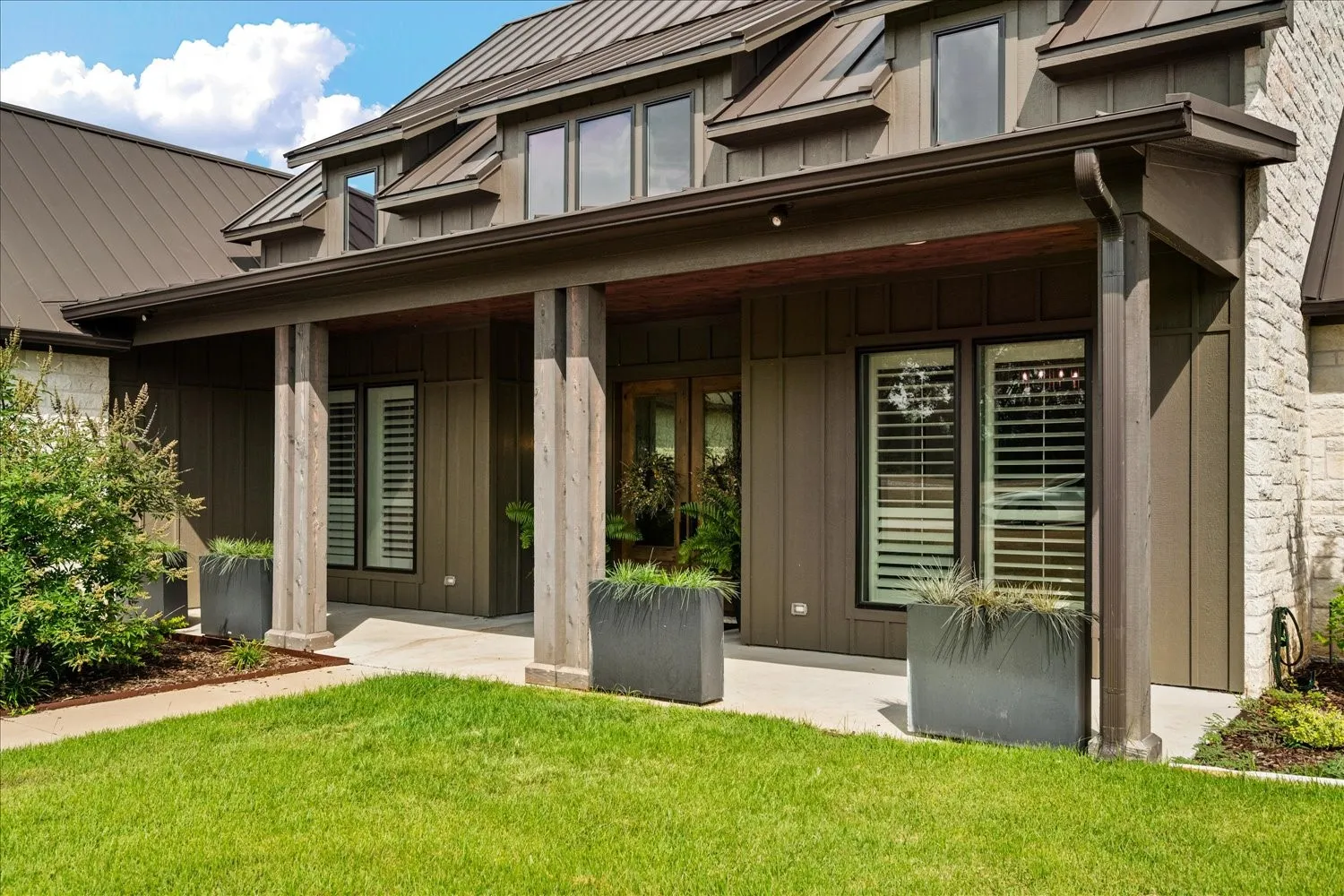 Contemporary exterior with a metal roof, stone veneer accents, board and batten siding, and a covered porch supported by large columns