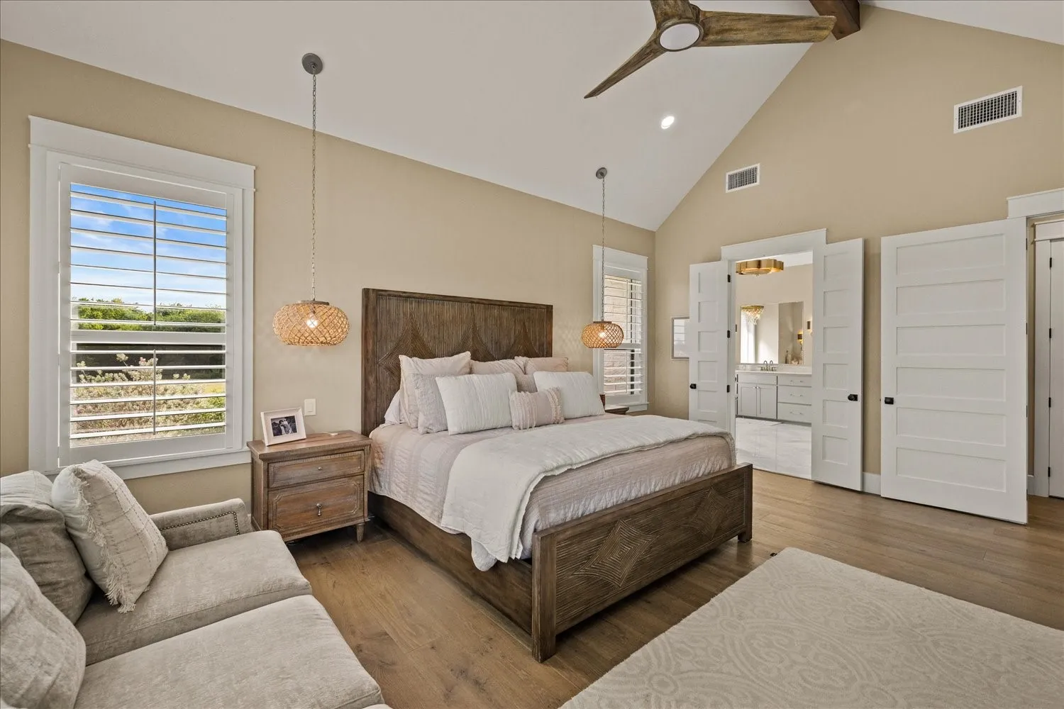Vaulted ceiling with wood-finish ceiling fan, wood-finish flooring, white plantation shutters, and pendant lighting