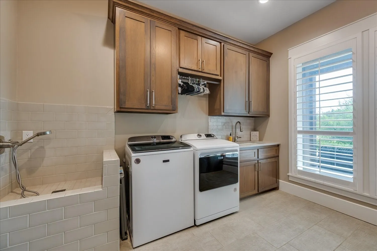 Laundry room featuring wood cabinetry, a utility sink, tiled backsplash, and a built-in pet bathing station with a handheld sprayer