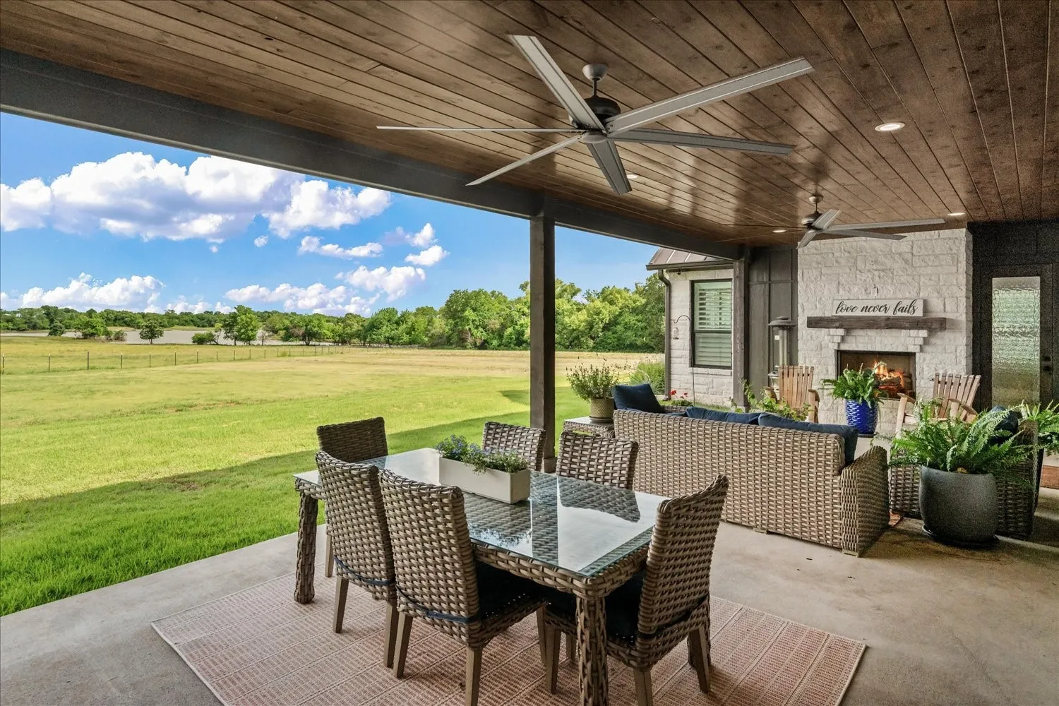 Covered patio featuring a wood-paneled ceiling, multiple ceiling fans, and an outdoor fireplace with a stone surround
