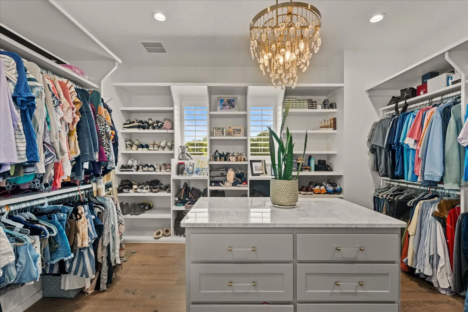 Custom closet system featuring wood-finish flooring, built-in shelving, hanging rods, and a central island with a light-toned countertop