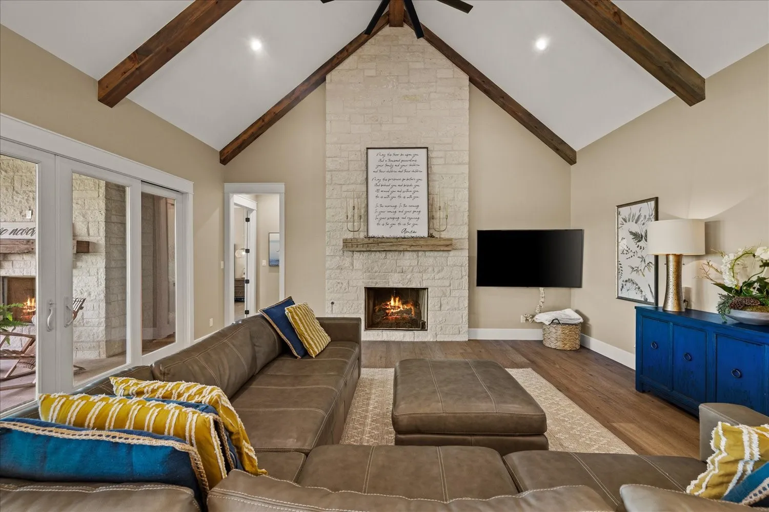 Vaulted ceiling with exposed wood beams, stone-clad fireplace, wood-finish flooring, and double glass doors