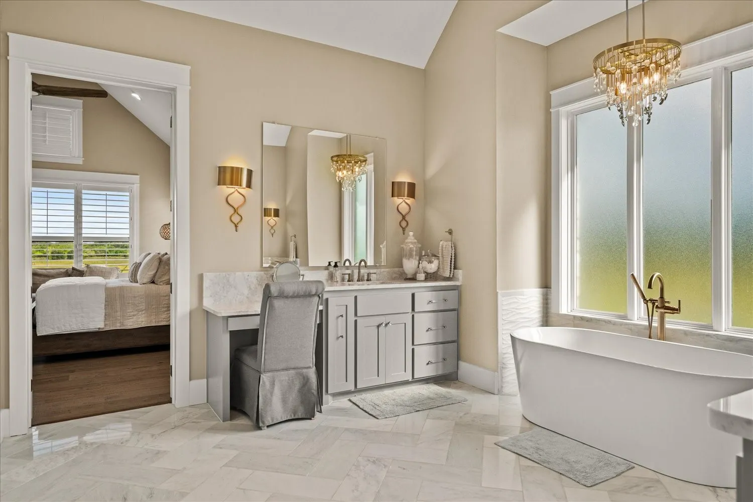 Marble-look tile flooring, free-standing soaking tub with a floor-mounted faucet, vanity with integrated sink and mirrors, and a vanity dressing table