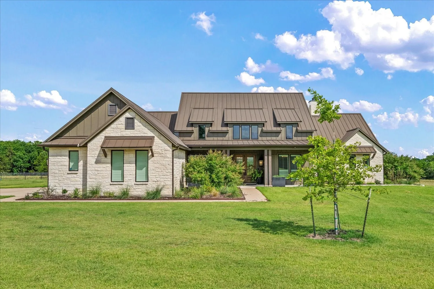 Stone facade with board and batten gables, metal roof, covered entry, and expansive lawn