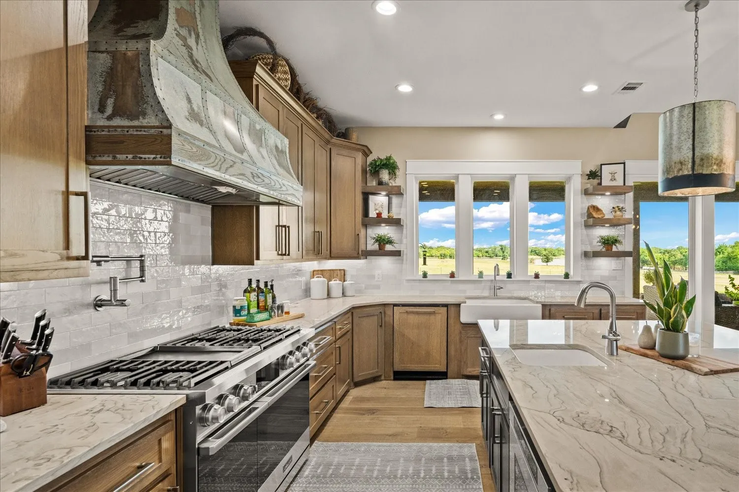 Gourmet kitchen featuring a commercial-style range, custom range hood, patterned tile backsplash, farmhouse sink, and light wood-finish cabinetry