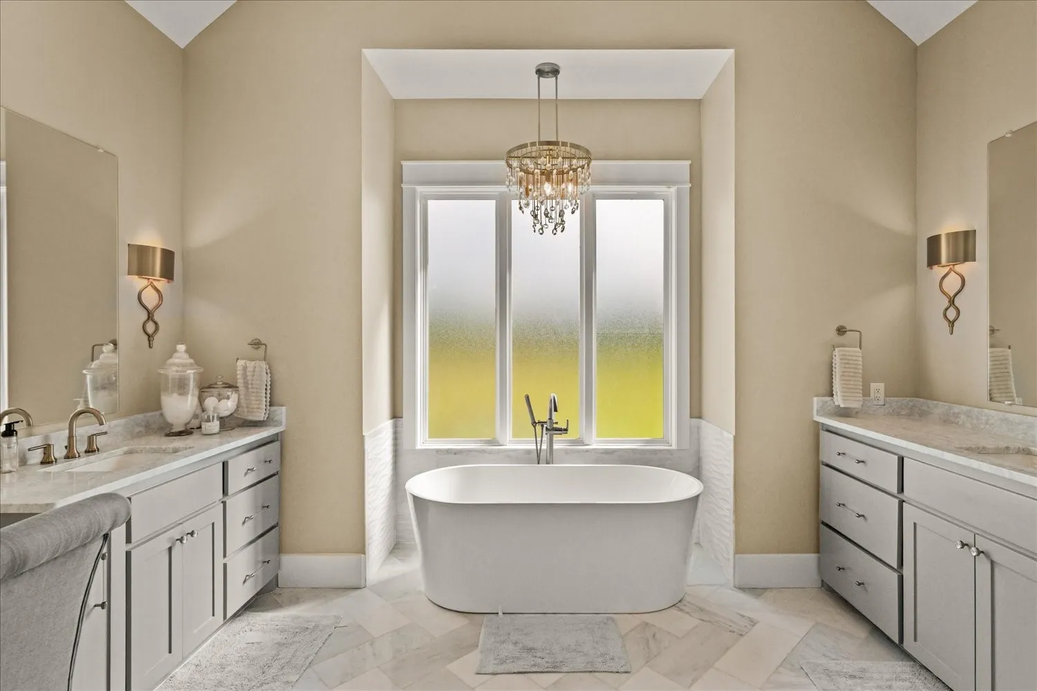 Freestanding soaking tub, dual vanity with undermount sinks, stone countertops, brushed nickel fixtures, and a decorative chandelier