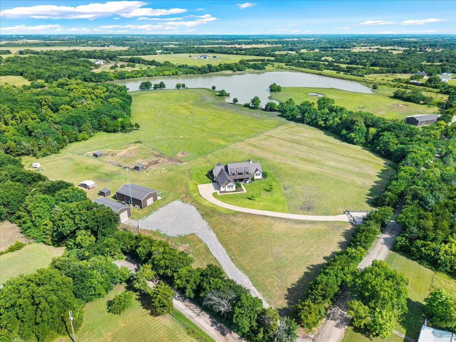 Expansive rural property featuring a large home, multiple outbuildings, circular driveway, and a substantial body of water