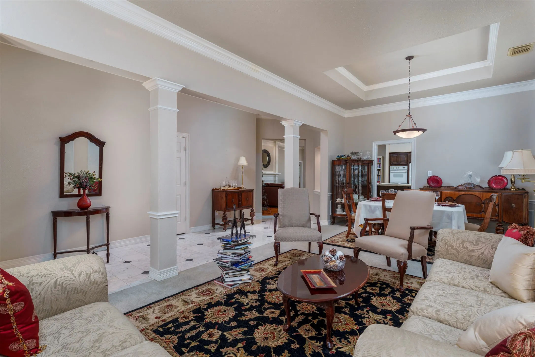 Tray ceiling with a pendant light fixture, cased openings, crown molding, and columns