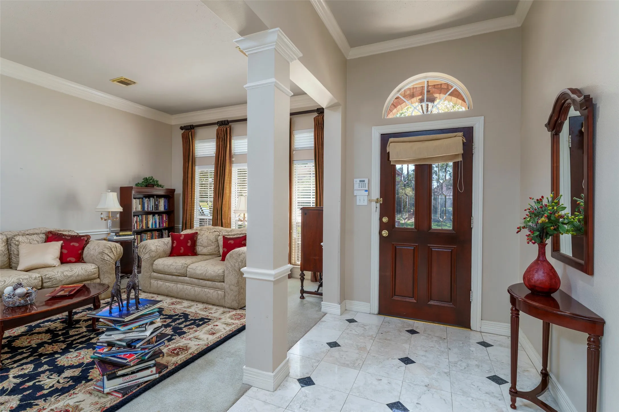 Entryway featuring a rich wood-paneled door with glass inserts, an arched transom window, and tiled flooring with dark square accents