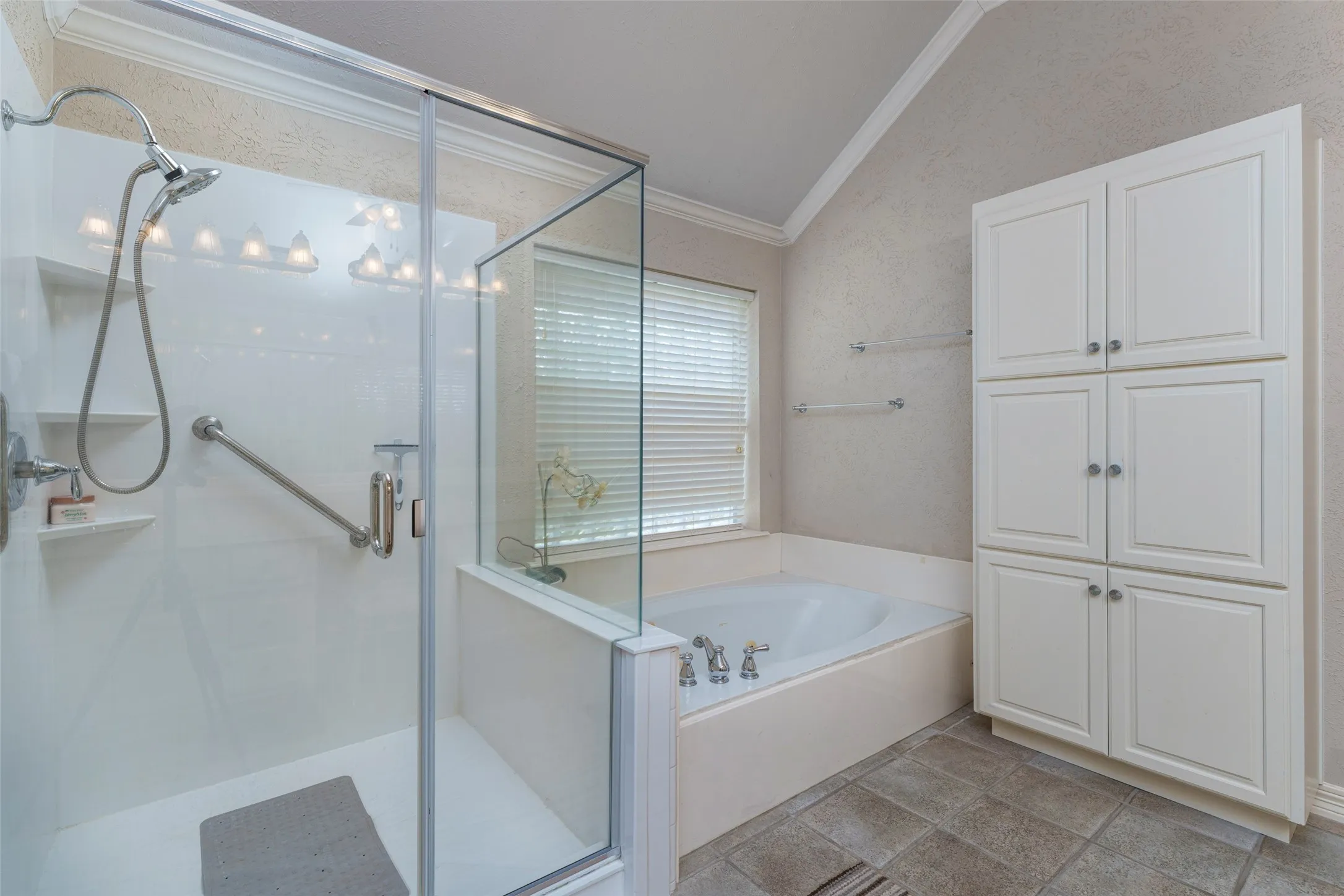 Glass-enclosed shower with a handheld shower head, built-in corner tub, built-in cabinetry, and tile flooring