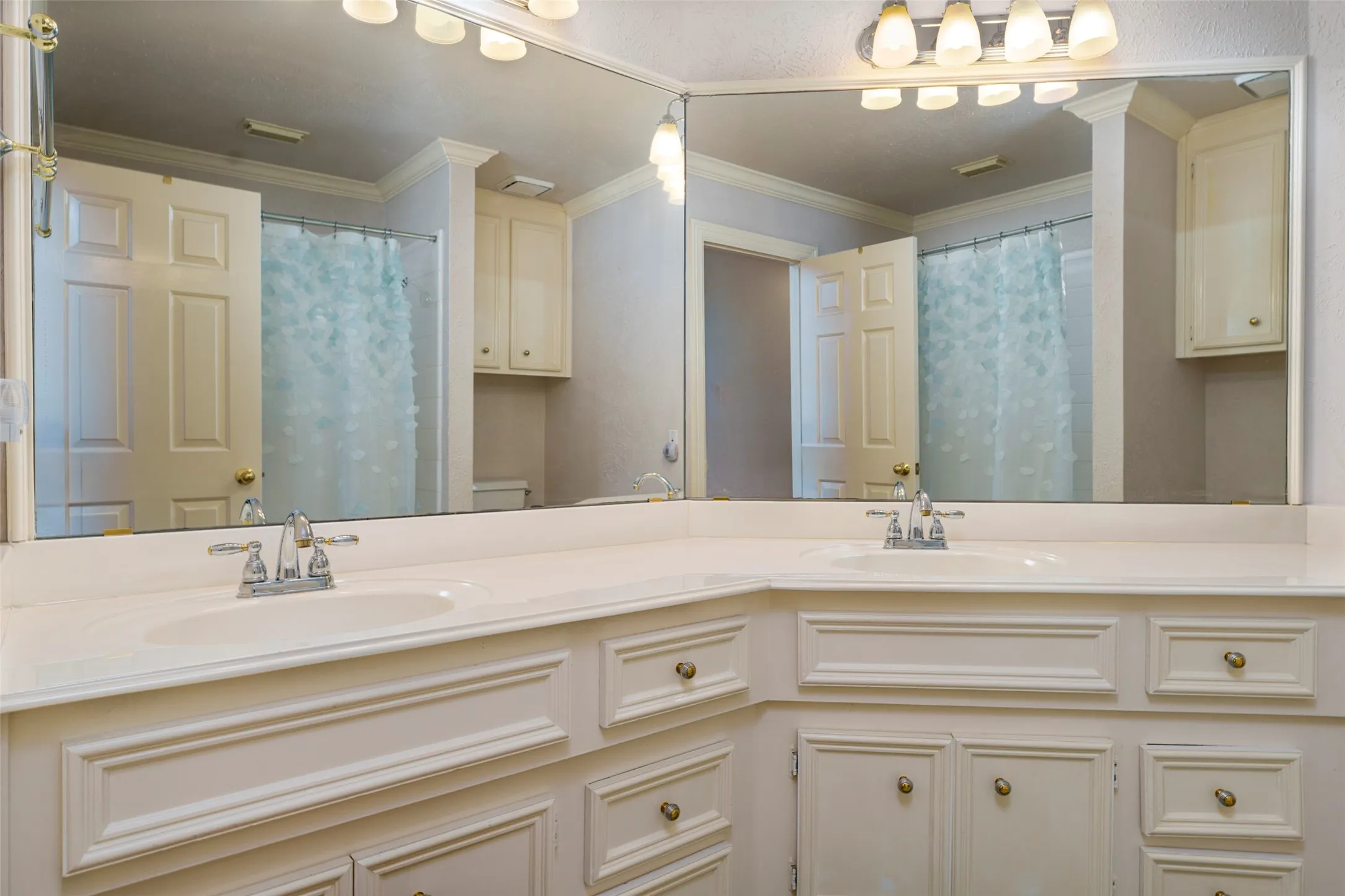Double vanity with integrated sinks, extensive built-in cabinetry, large wall-mounted mirror, and overhead vanity lighting