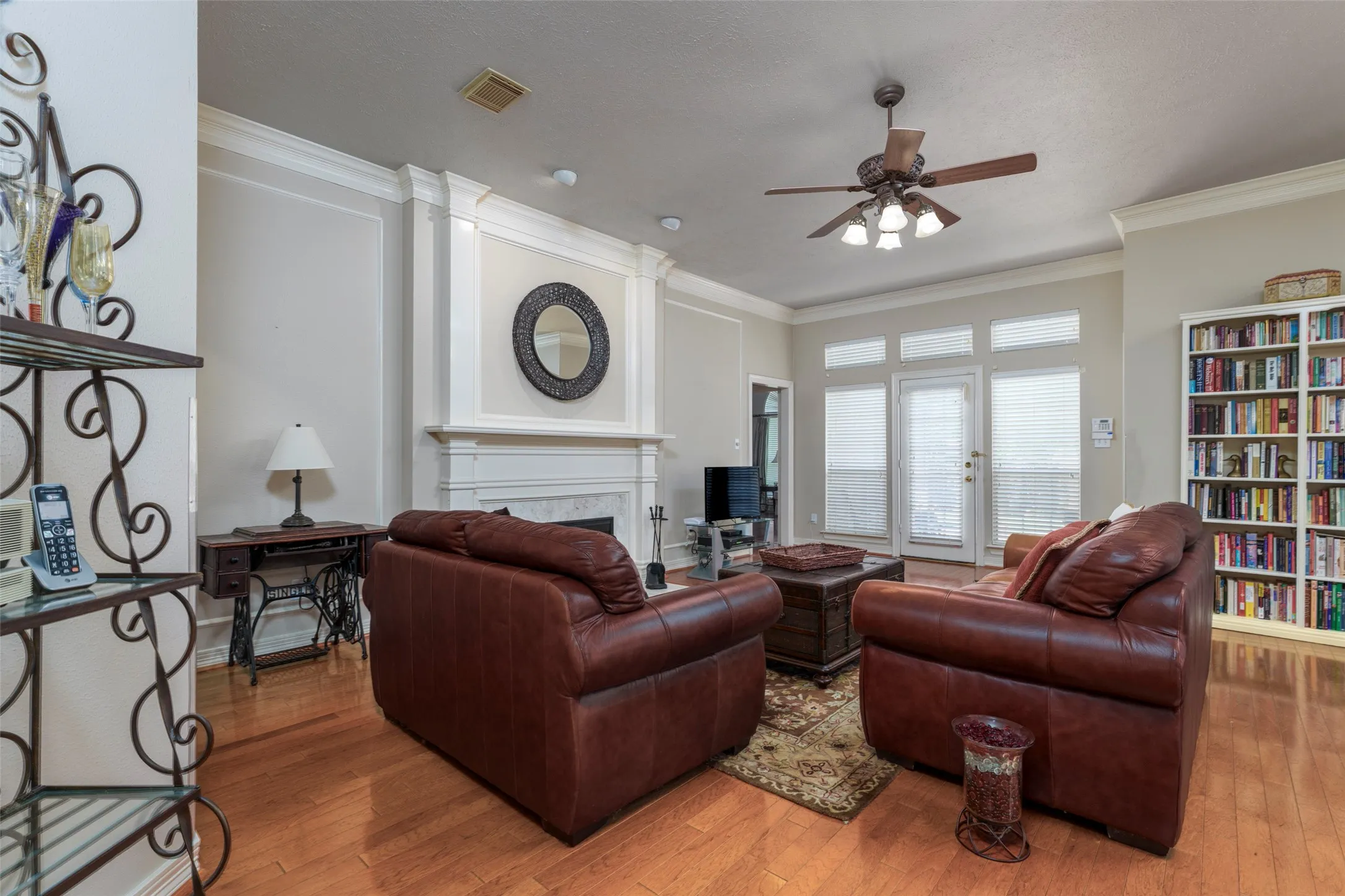 Hardwood-finish flooring throughout, a ceiling fan with integrated lighting, built-in shelving, and a prominent fireplace with a decorative mantelpiece