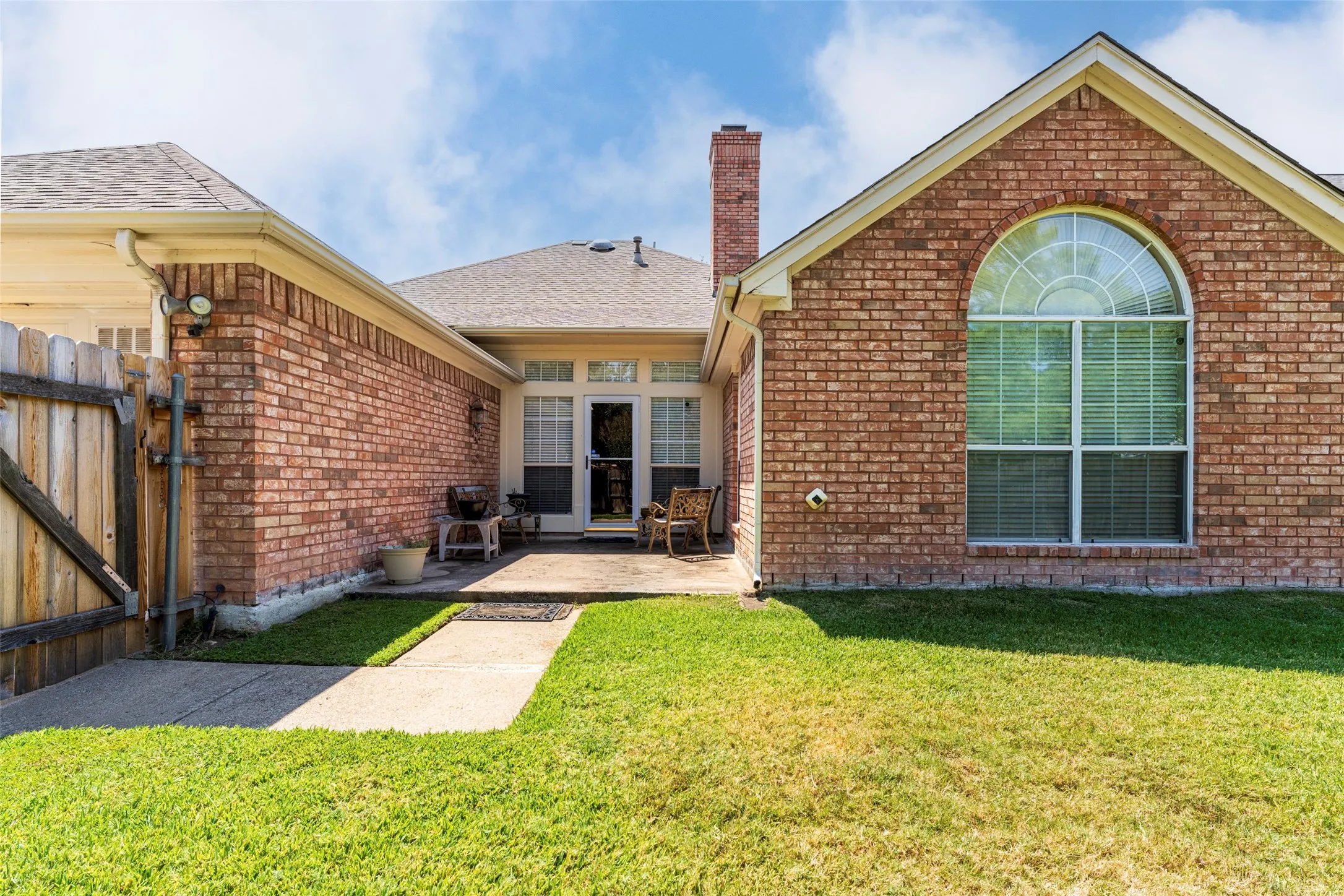 Brick exterior with a prominent arched window, a brick chimney, and a concrete patio
