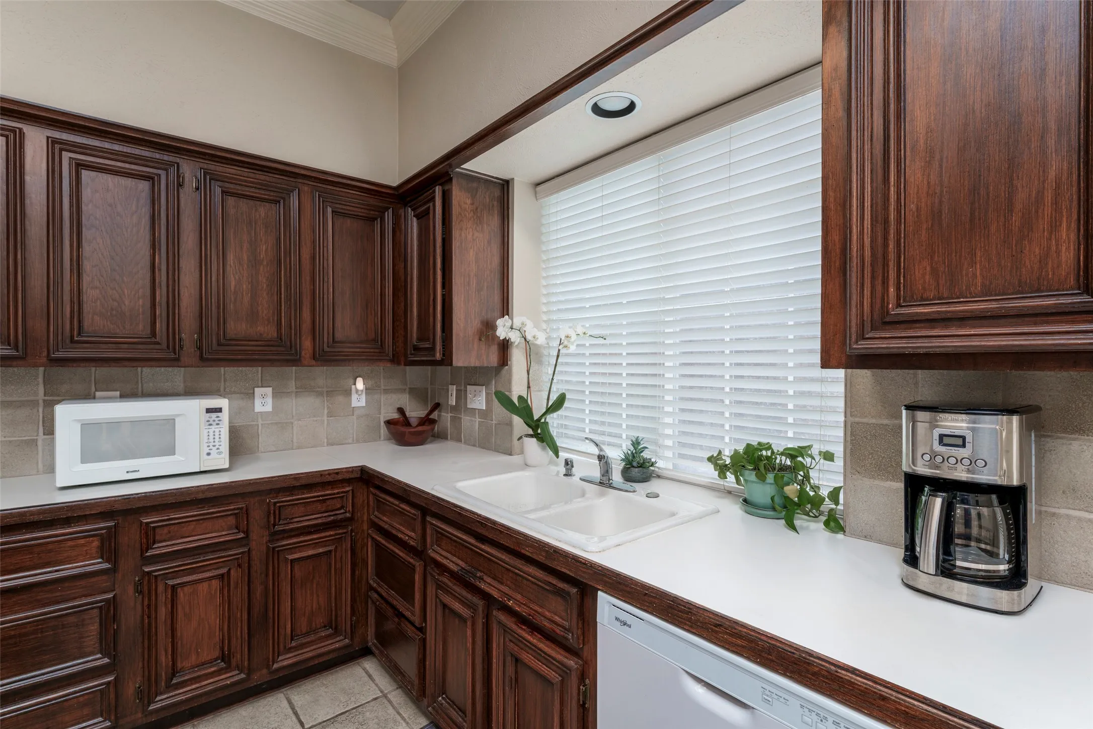 Rich wood cabinetry, white countertops, dual basin sink, tile backsplash, and recessed lighting